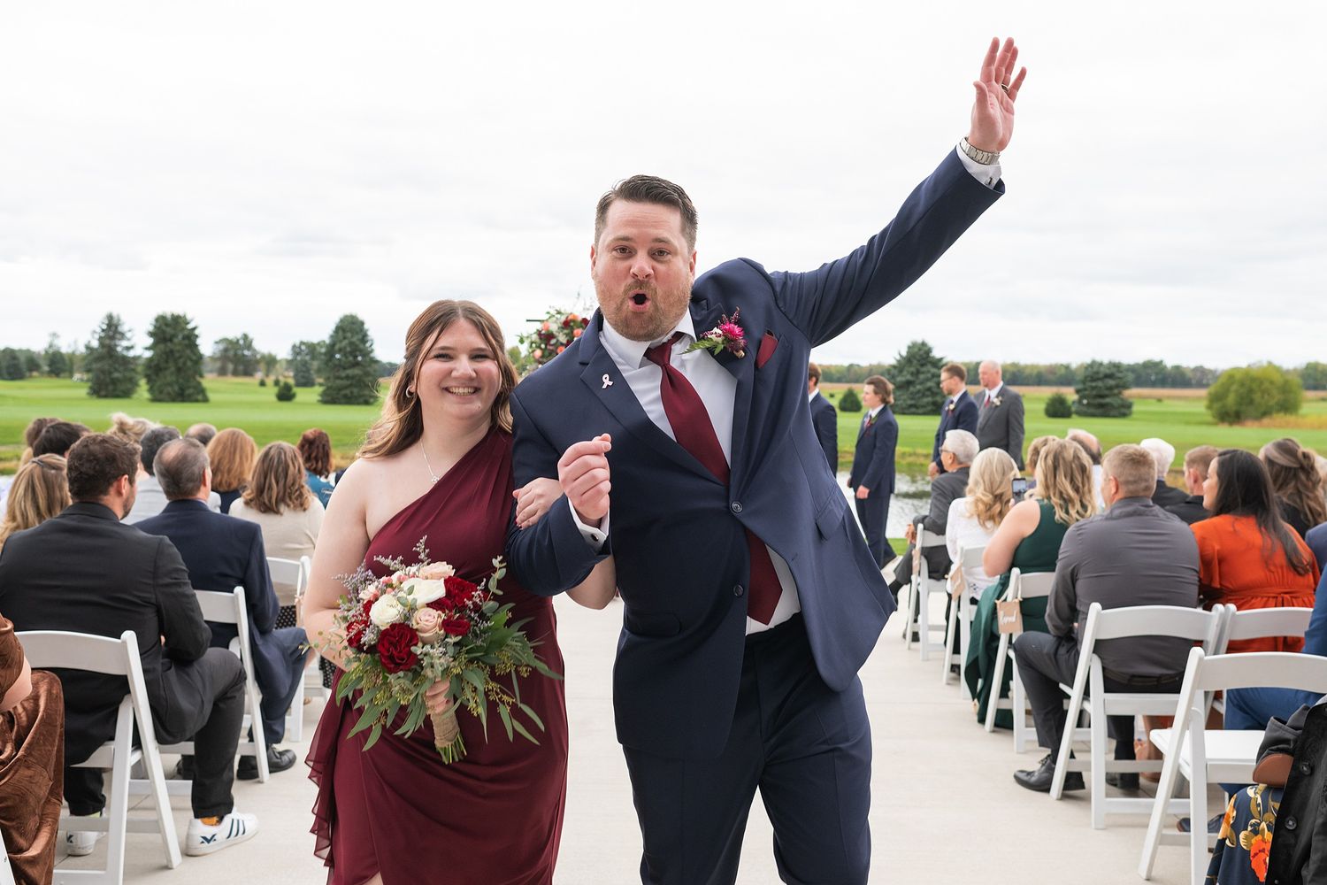 Newlywed couple celebrates joyfully while walking back down wedding aisle.