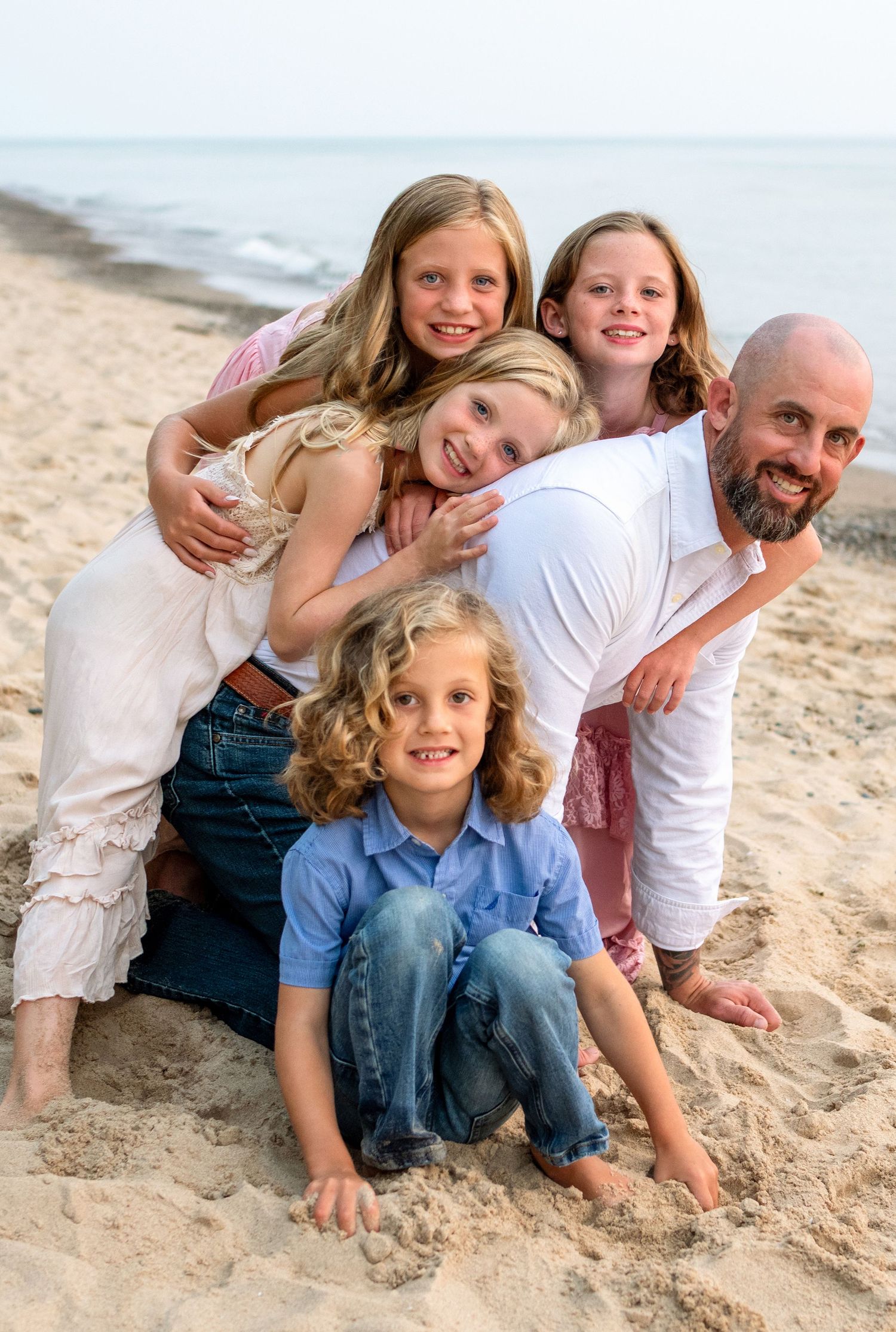 Family of five posing together on a sandy beach, with parents and three children smiling for a portrait near the ocean.