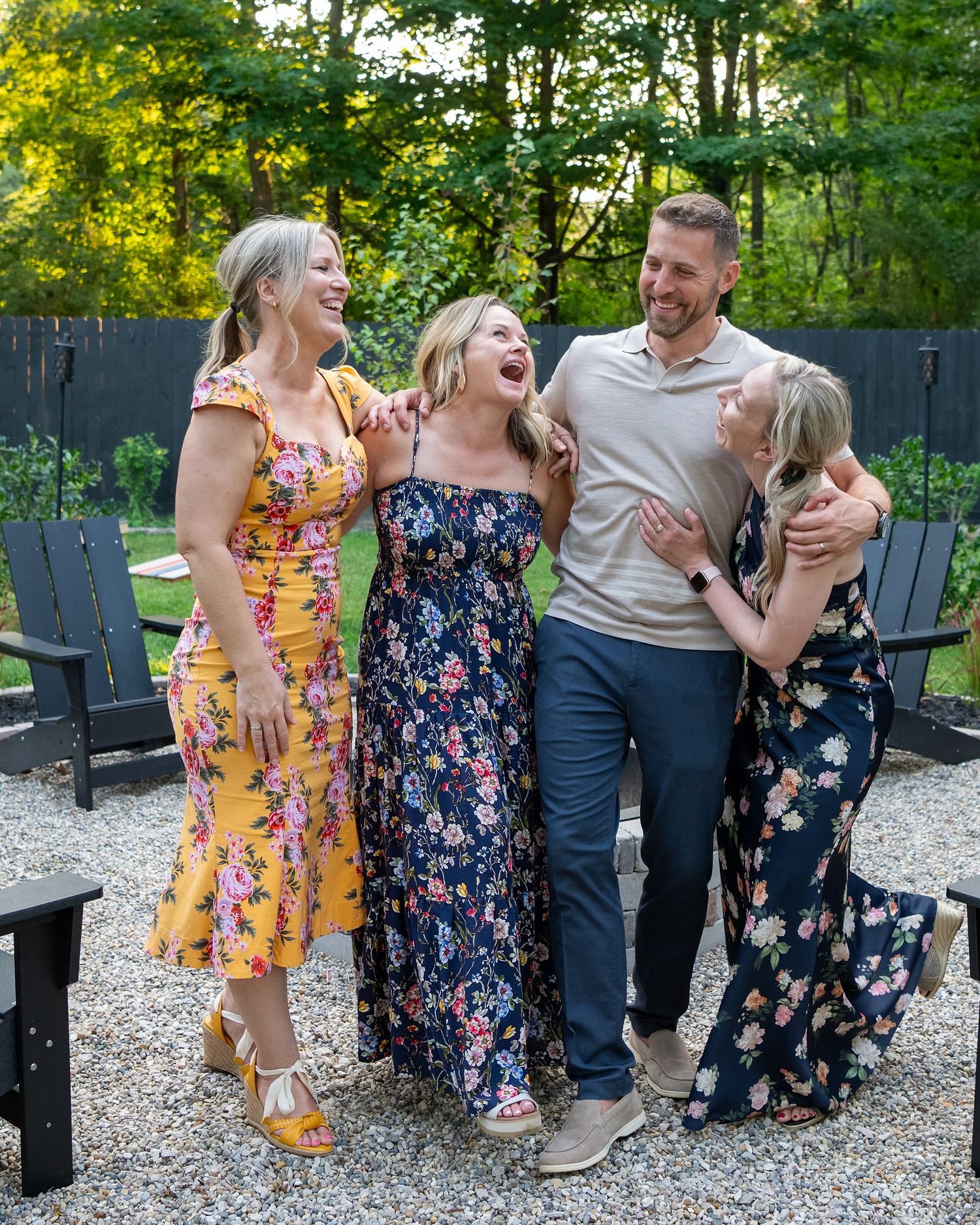 A group shares joyful laughter while relaxing together on Adirondack chairs in a backyard garden setting at sunset.