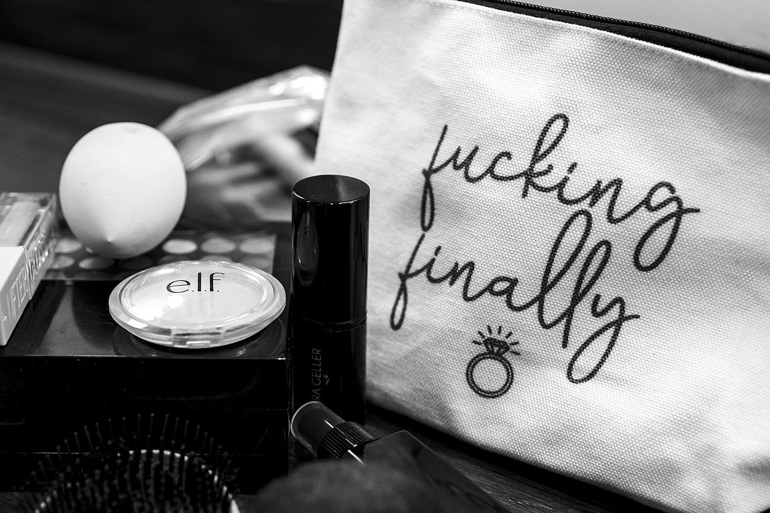 Black and white photo of elf makeup compact, brush, and a bride-to-be cosmetic bag reading fucking finally with ring.