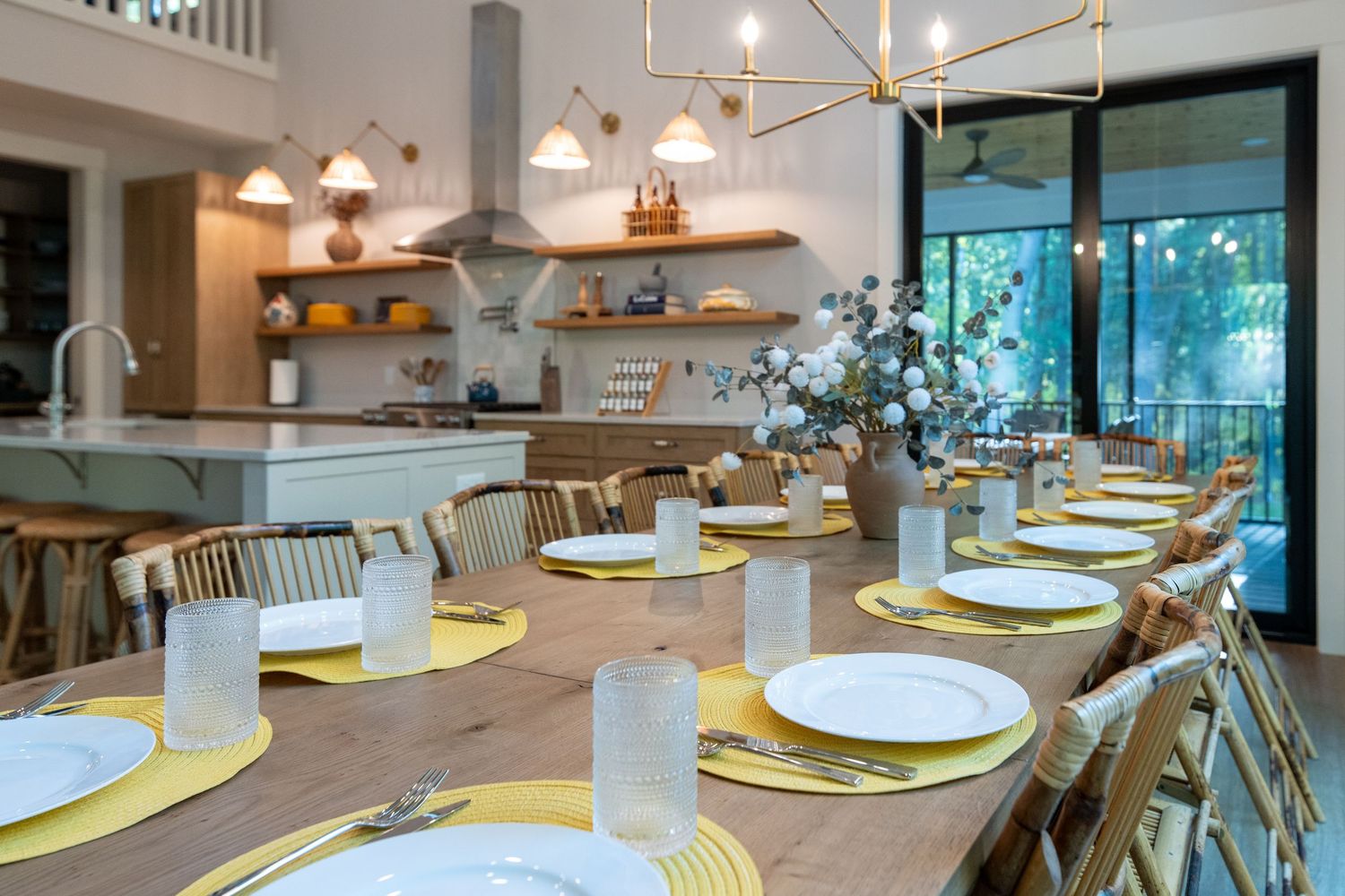 Elegant dining room with yellow placemats, white plates, and gold chandelier adjacent to a modern open kitchen.