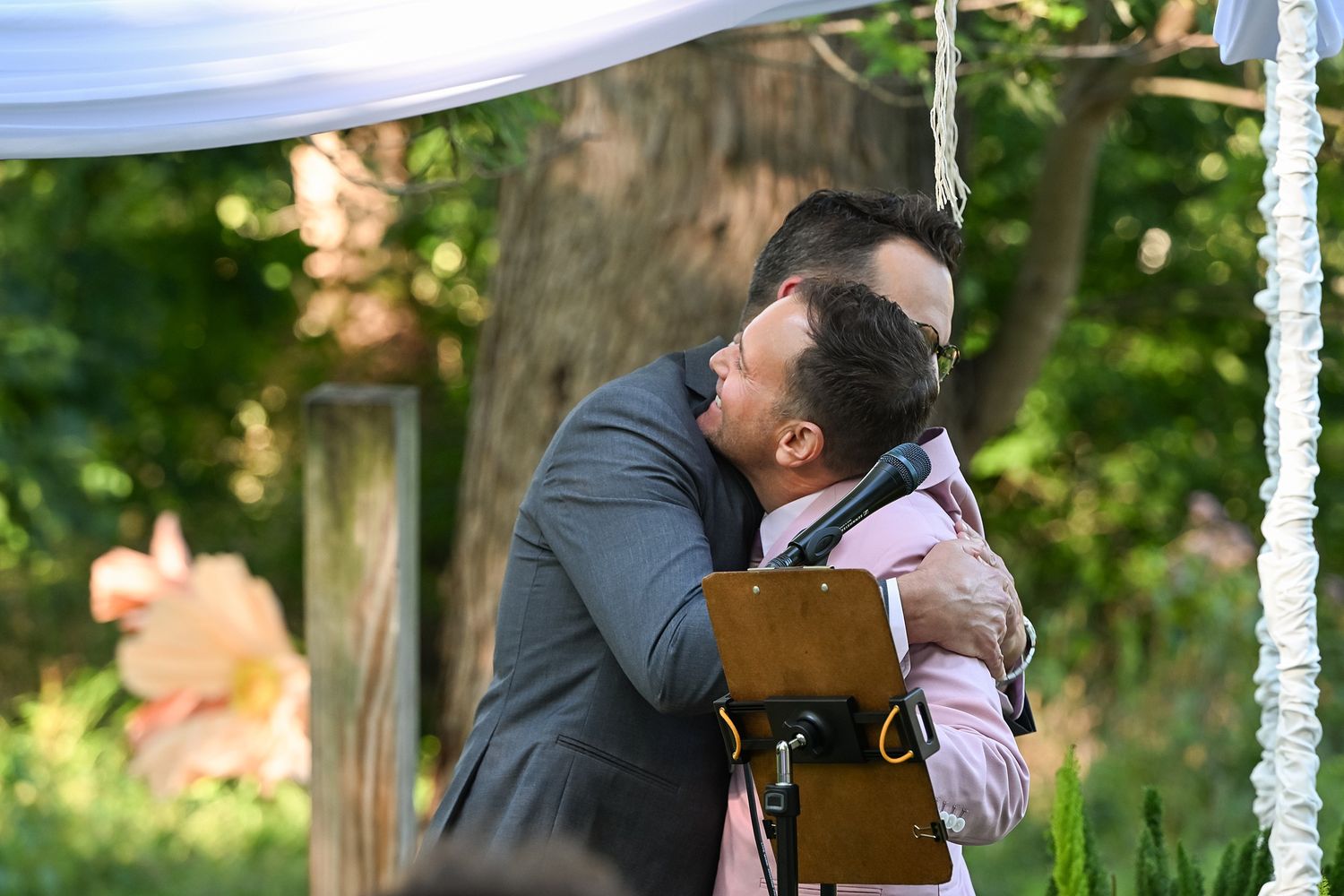 A couple in formal attire shares a romantic kiss under a string of lights at an outdoor wedding celebration.