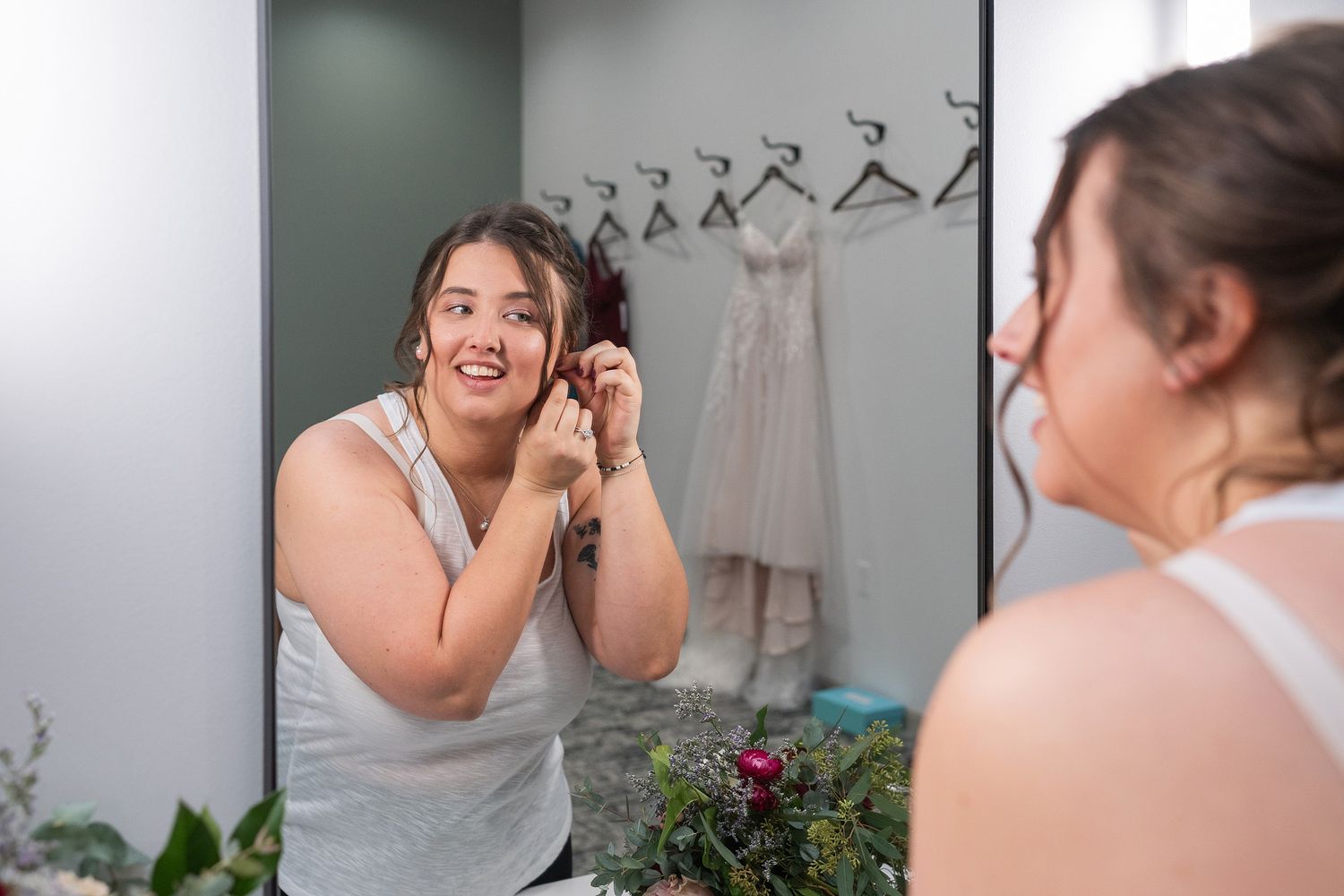 Bride putting on earrings while looking in mirror before wedding ceremony.