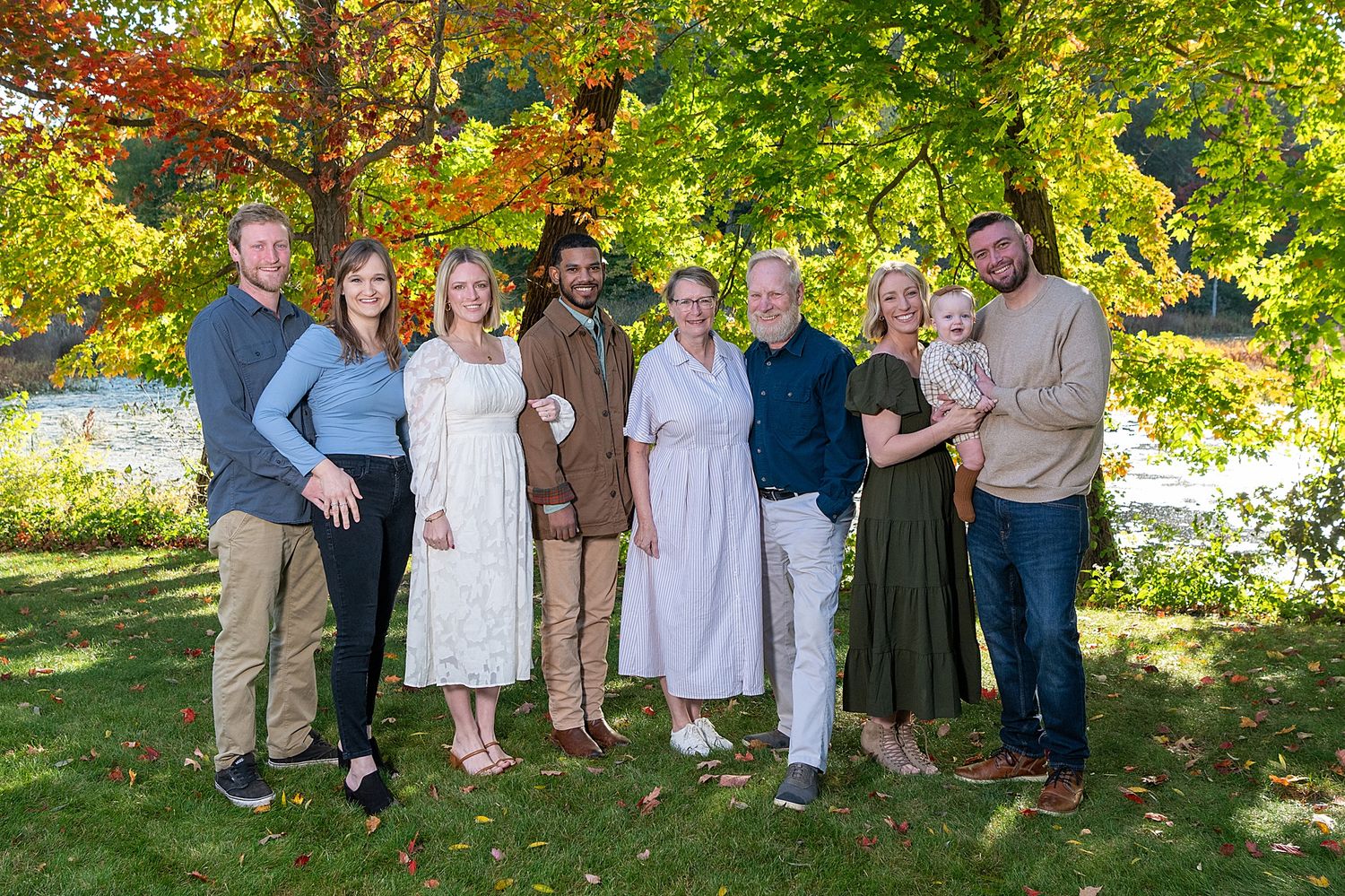 A large group poses for a casual outdoor portrait under vibrant fall foliage.
