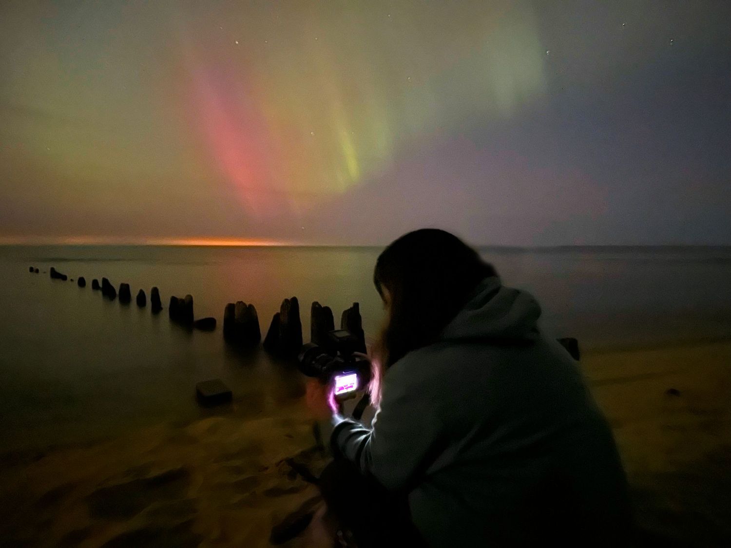 Colorful aurora borealis lights dancing in night sky over dark silhouetted structures.
