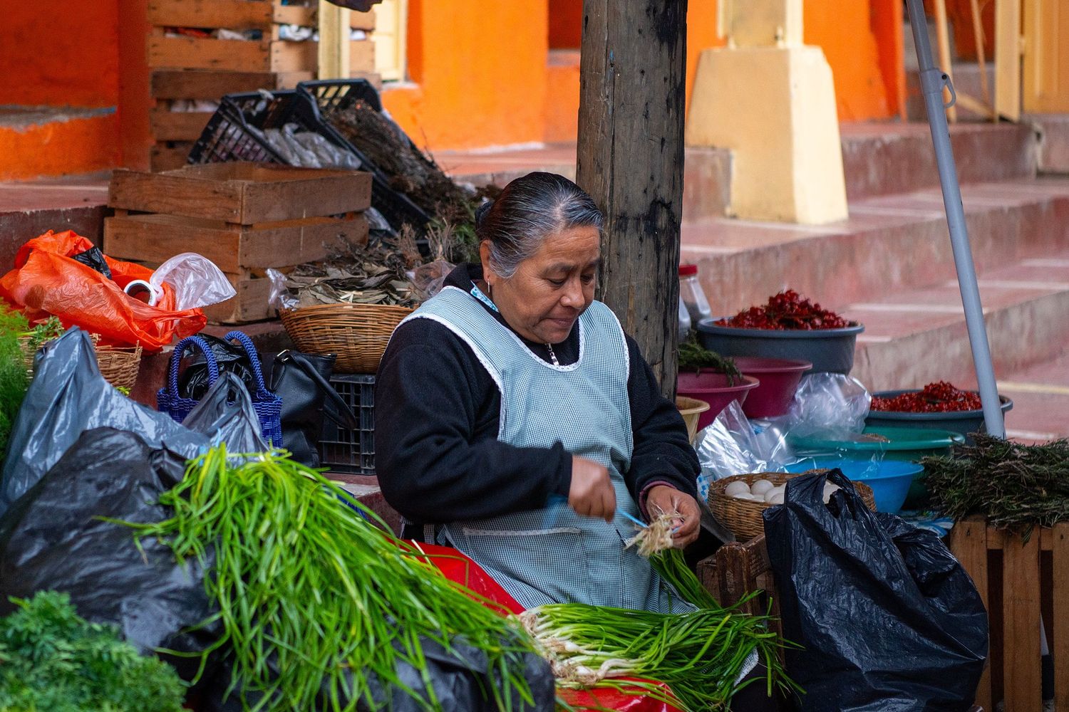 Fresh produce and vegetables displayed at outdoor market stalls with orange wall backdrop.