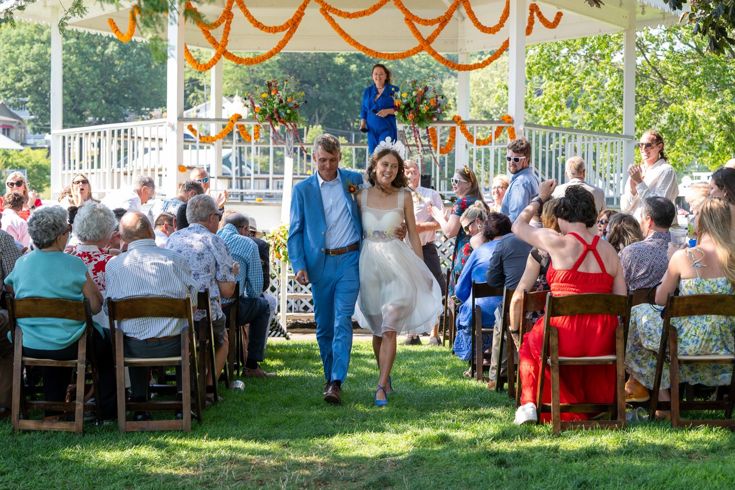 Outdoor wedding reception with orange decorations and guests seated in white chairs.