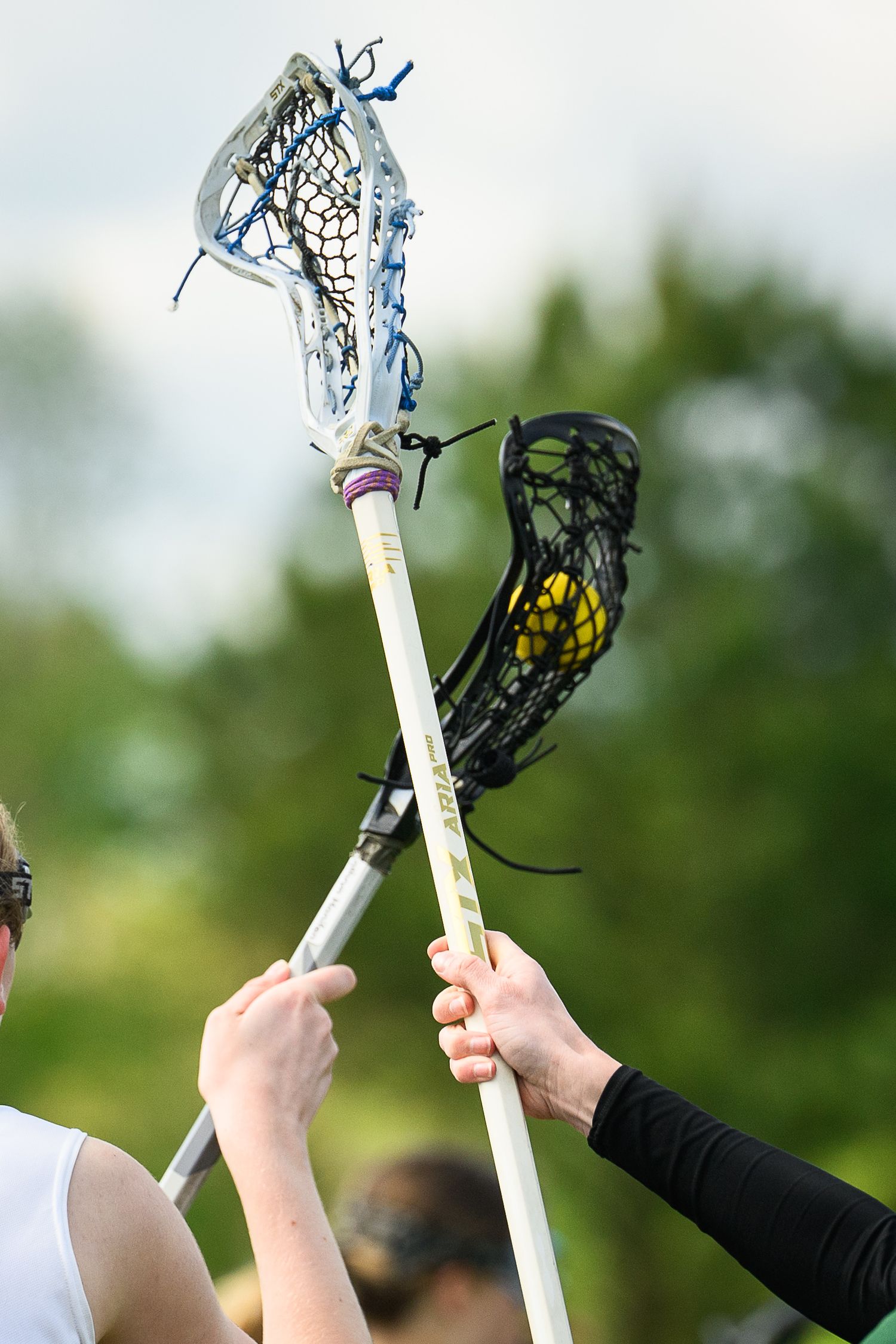 Two players compete for possession with lacrosse sticks raised during a womens lacrosse game outdoors.