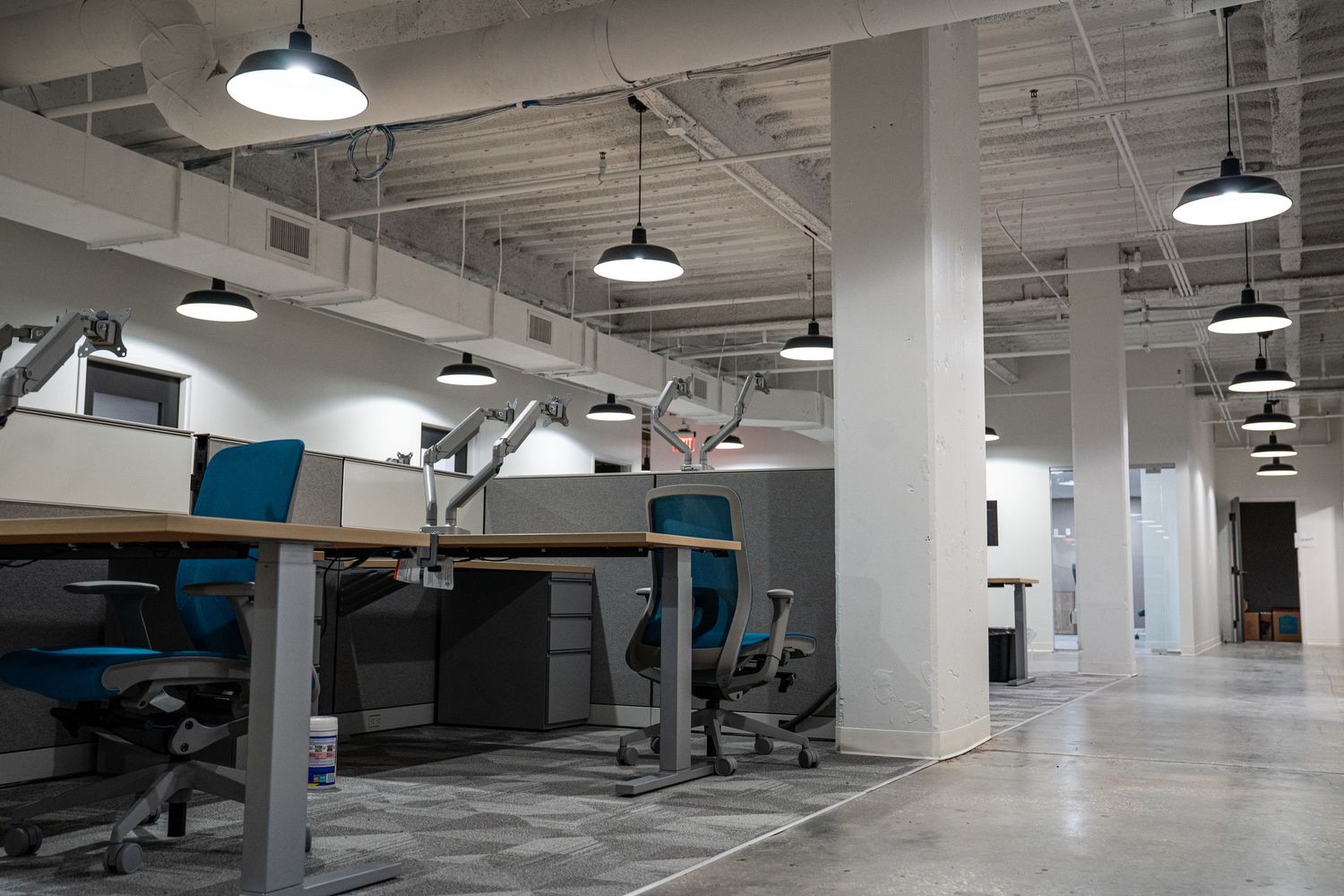 Modern office space with exposed ceiling, pendant lighting, and white walls in an industrial style layout.