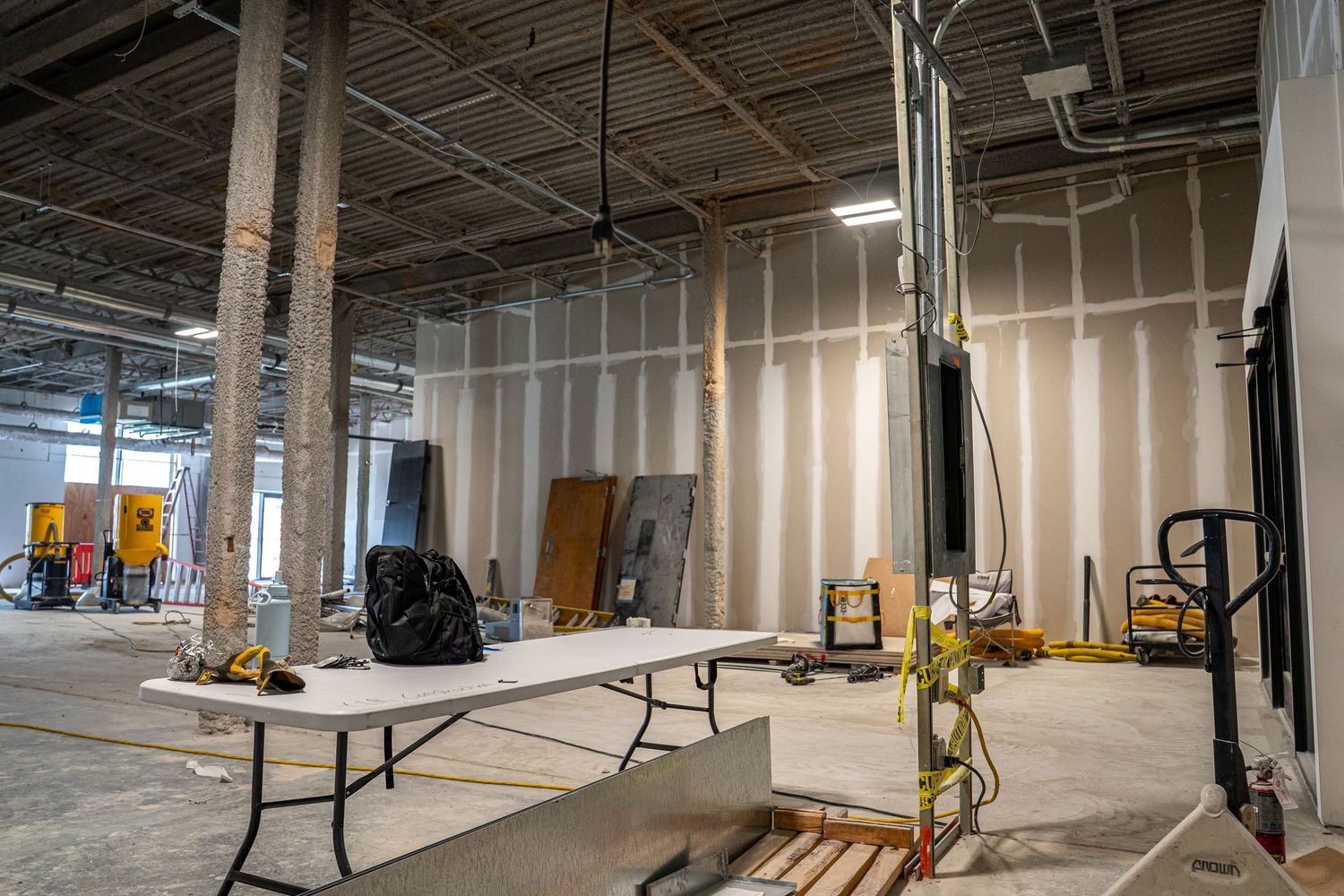 Commercial space renovation with folding tables and construction equipment scattered throughout.
