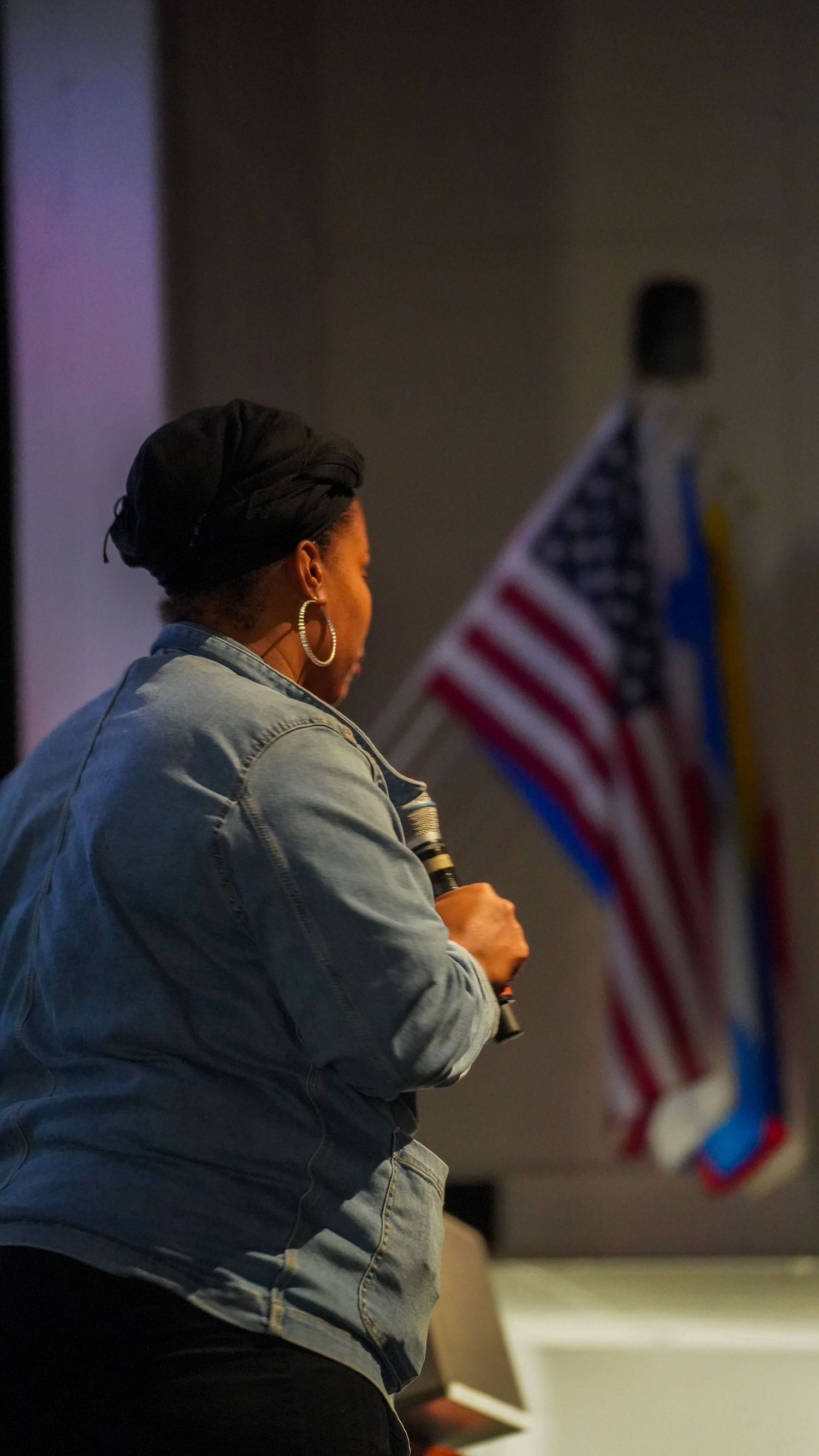 Speaker presents on stage with American flag visible in background.