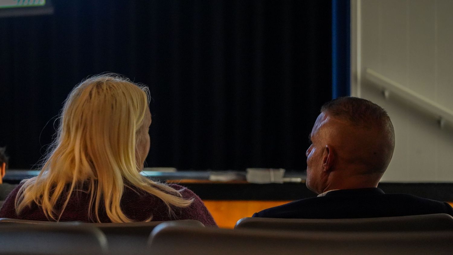 Two people sitting in theater seats viewed from behind during an event.