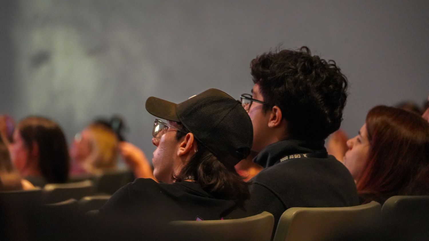Audience members watching intently in theater seats during a performance.