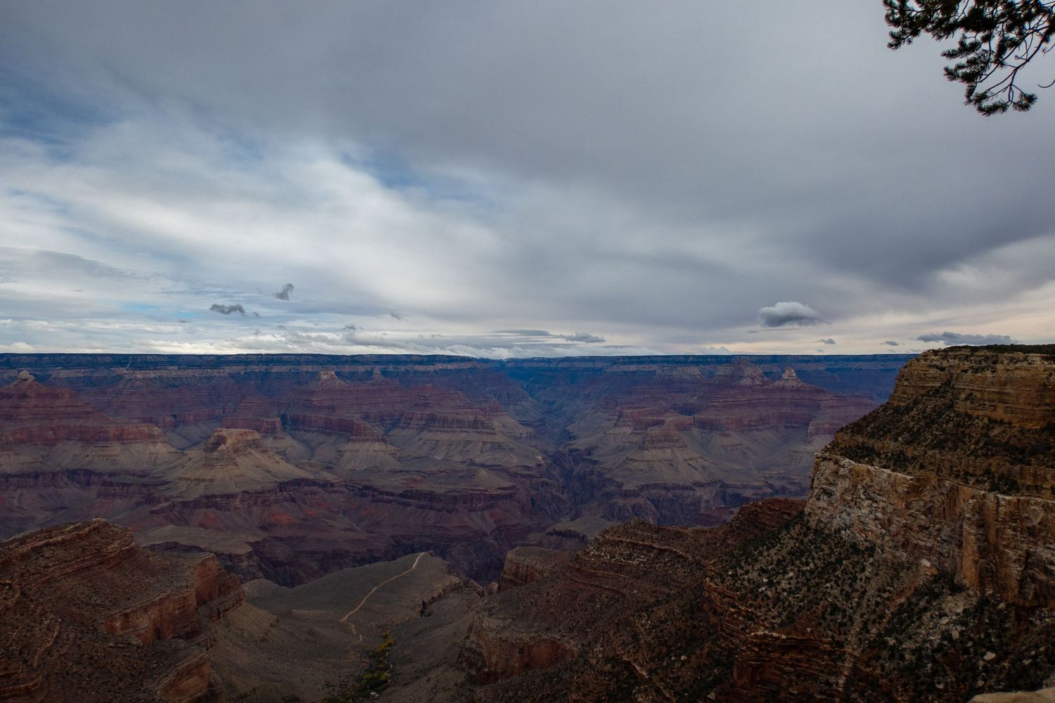 Dramatic cloudy skies stretch over the vast red rock formations of the Grand Canyon.