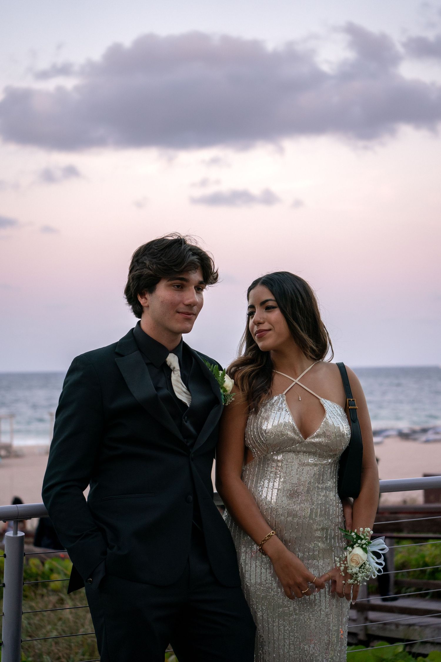 Couple in formal wear poses together against a sunset beach backdrop.