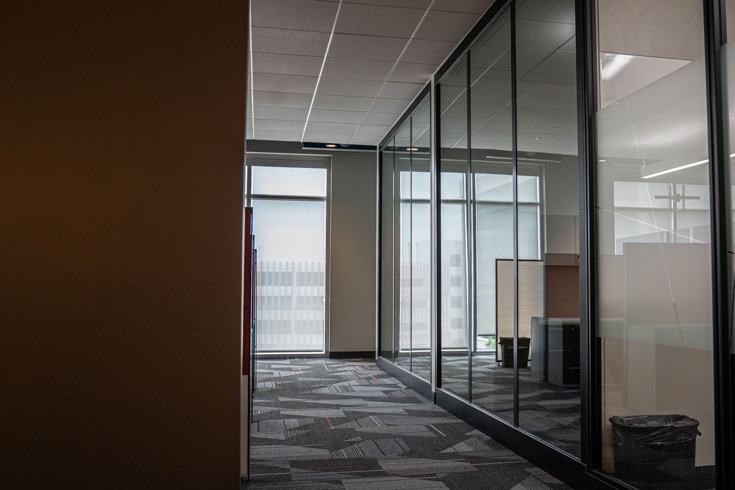 Empty commercial office space with floor-to-ceiling glass partitions and fluorescent lighting.