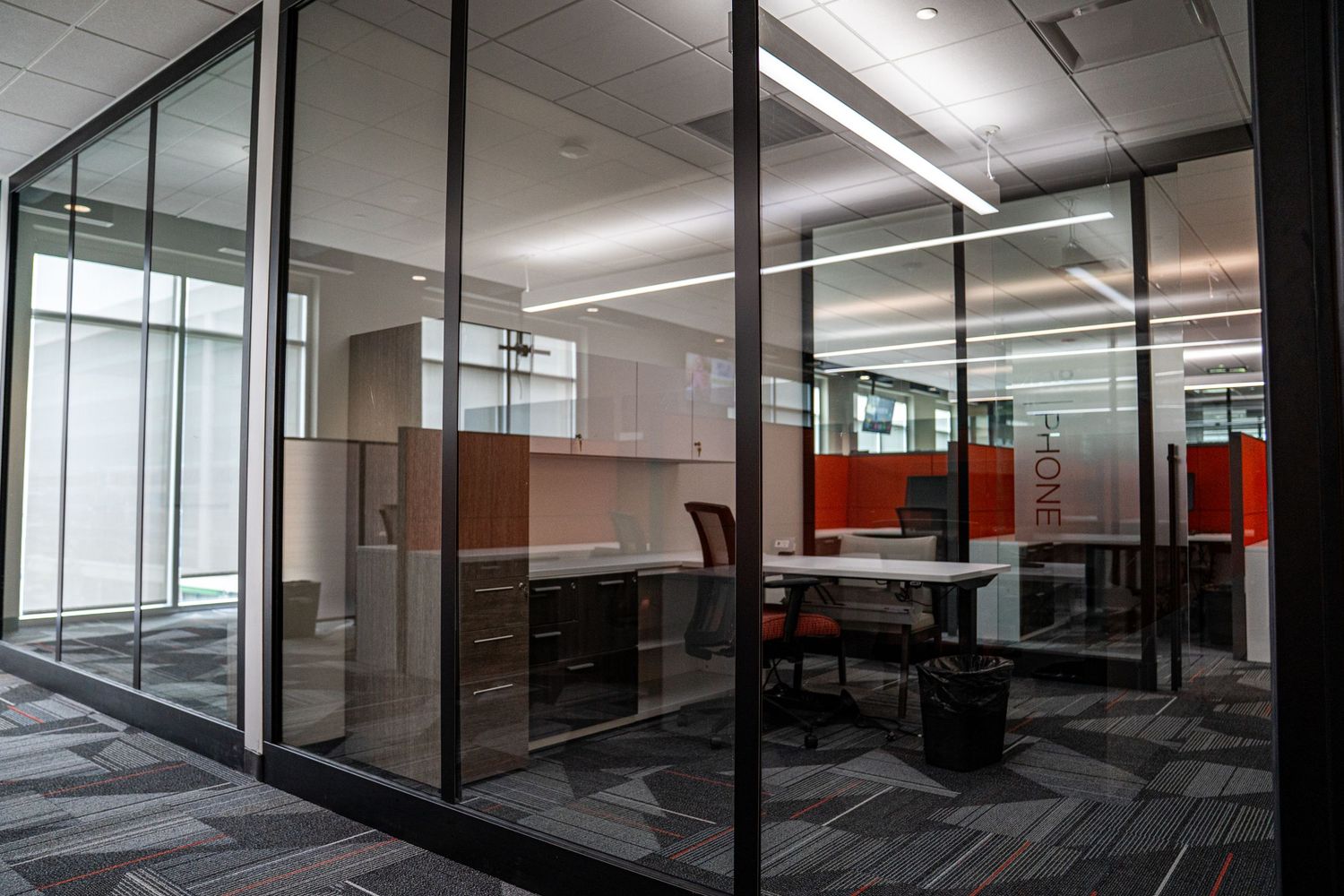 Open concept office space with glass partitions, red privacy panels, and modern desk arrangements.