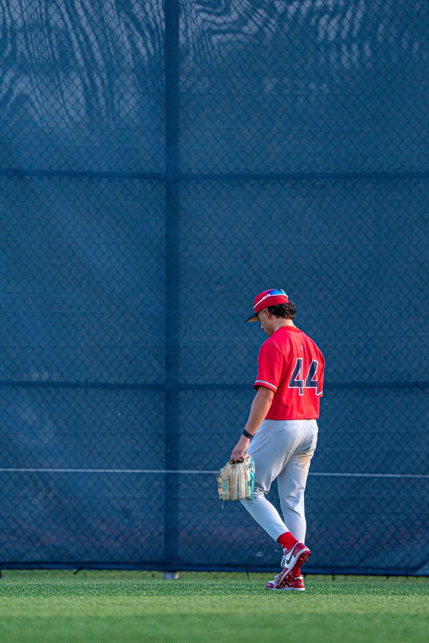 Baseball player wearing number 44 in red uniform walks across outfield during game.