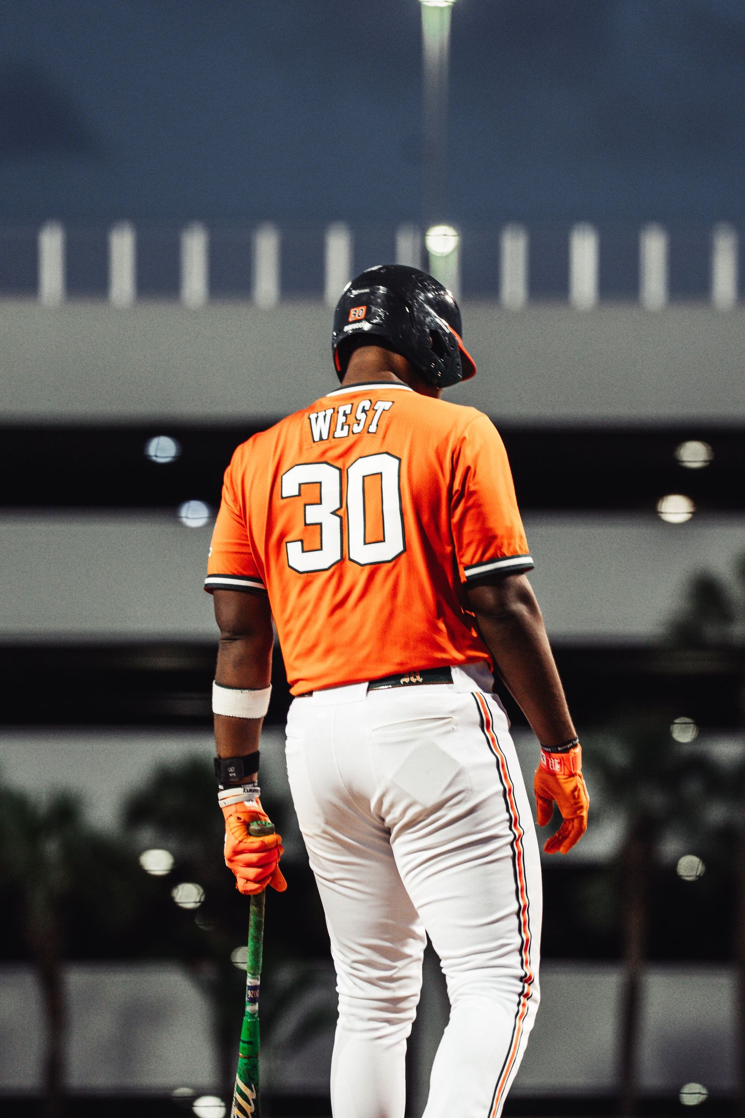 Baseball player West wearing number 30 orange jersey holds a bat on the field at night.