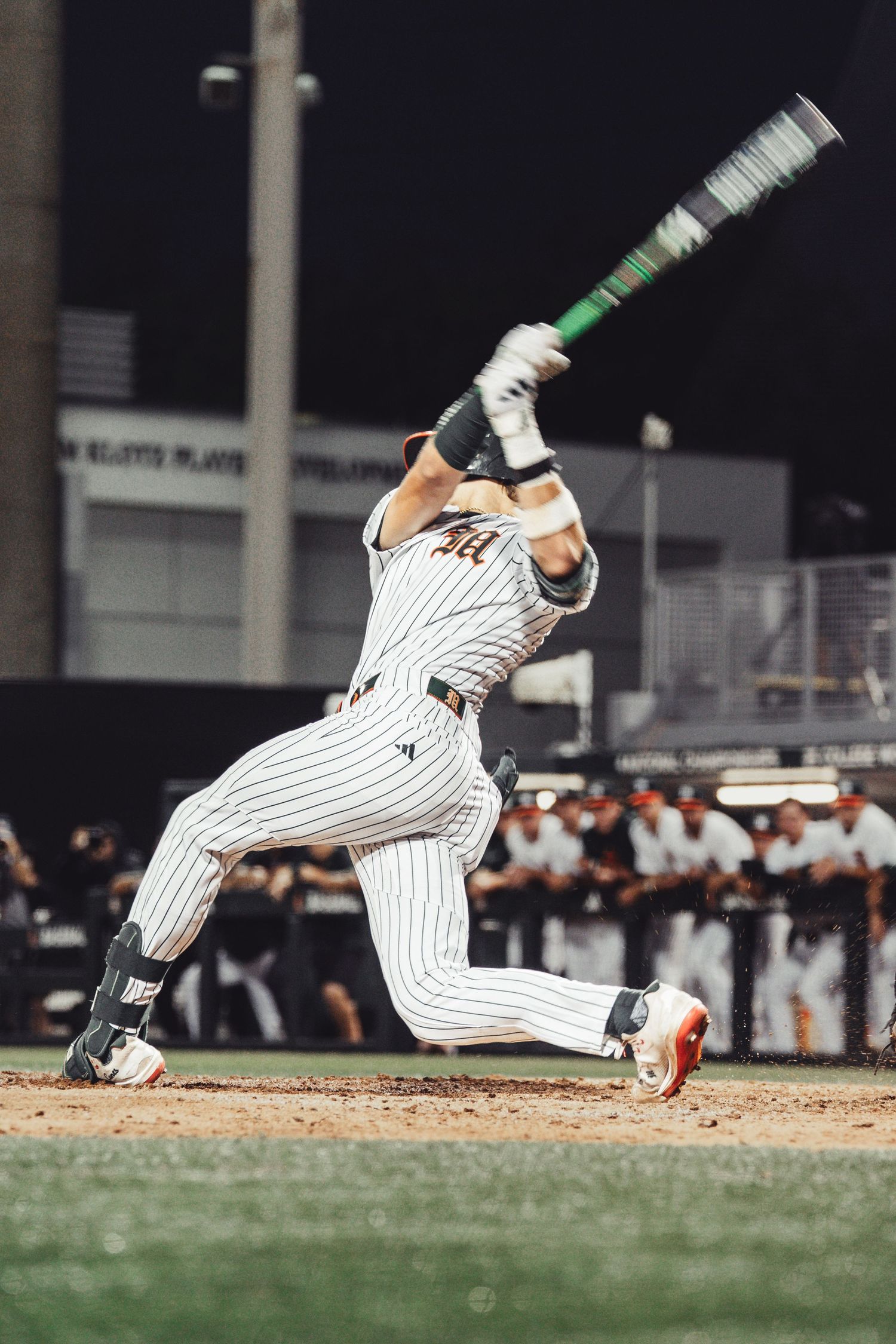 Baseball player in pinstripe uniform swinging bat during night game, captured in dynamic follow-through motion.