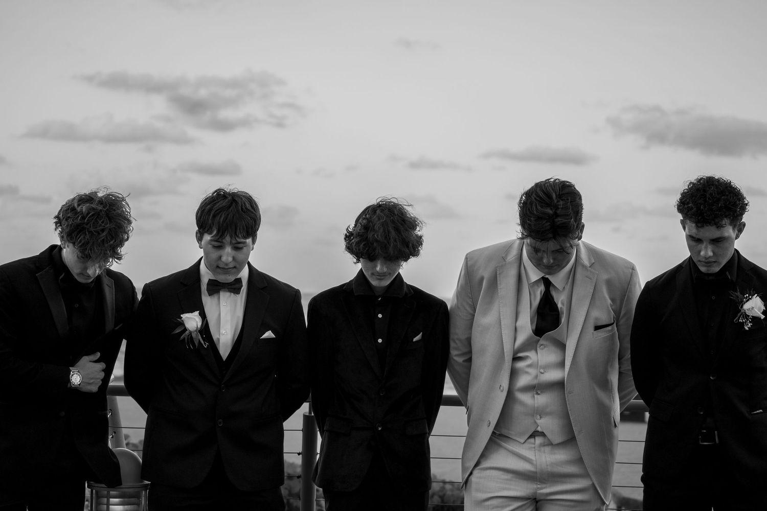 Group in formal attire poses together against cloudy sky backdrop.