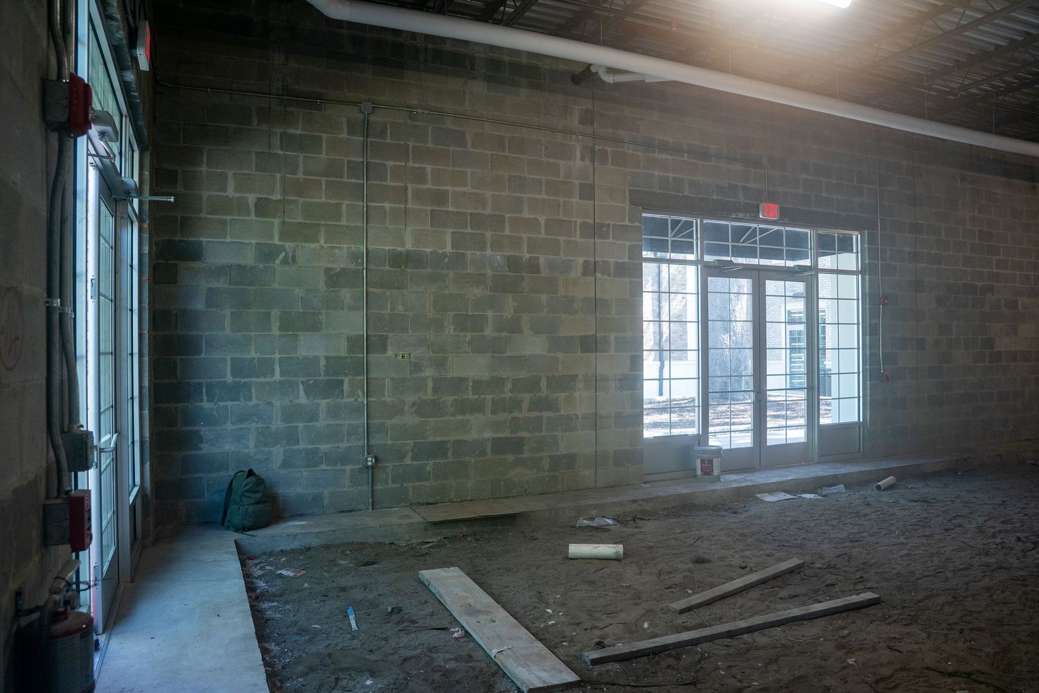 Commercial construction site interior with concrete block walls and large storefront windows.