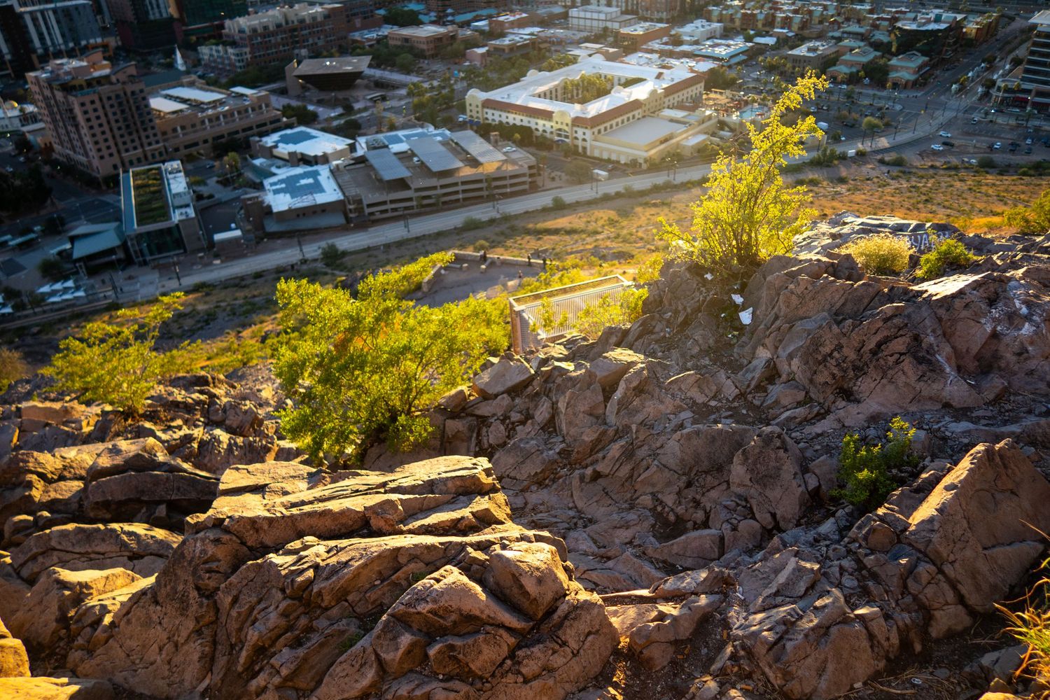 Urban landscape with buildings and roads viewed from elevated rocky terrain at sunset.
