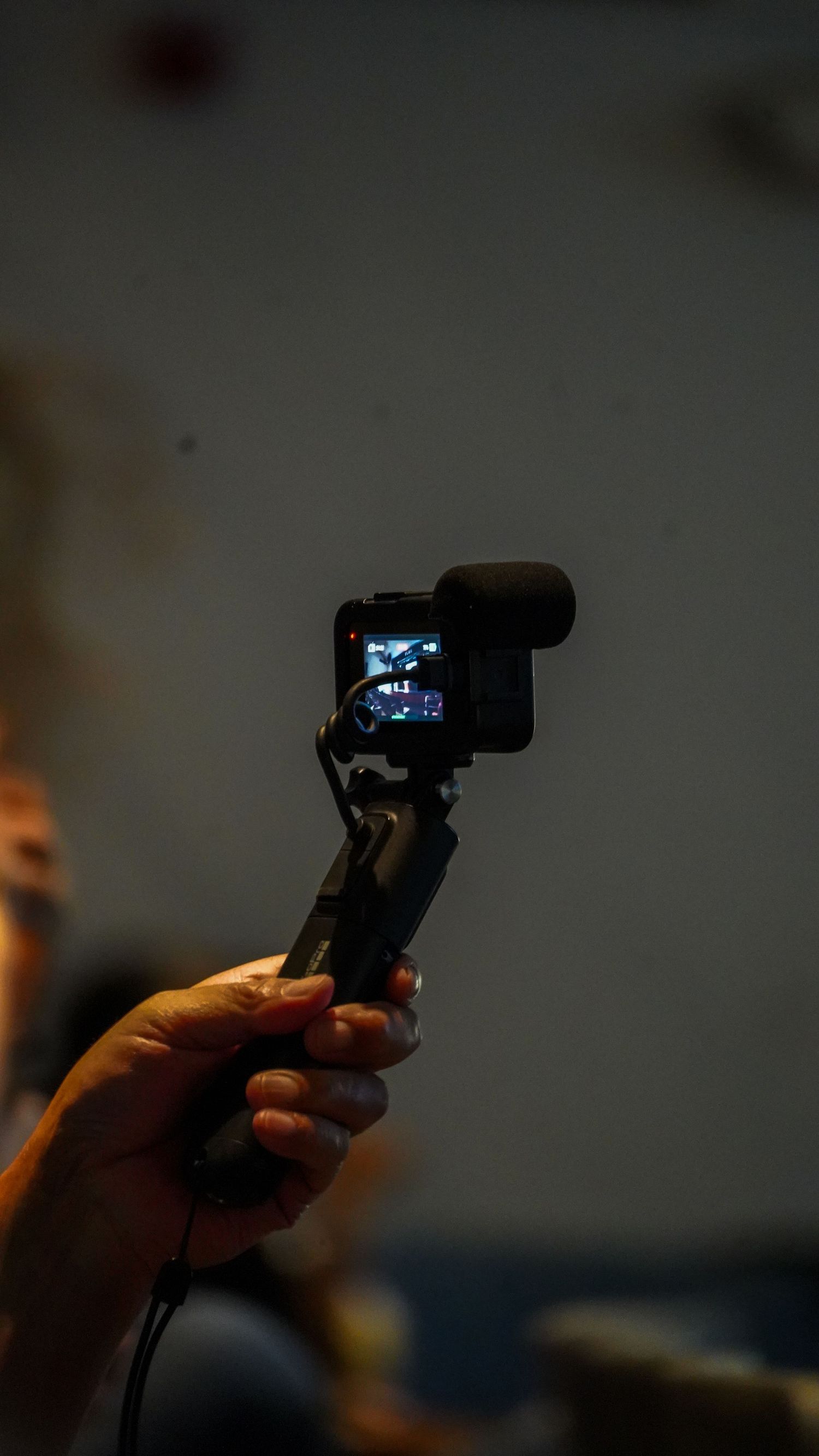 Hand holding a small camera or recording device in low light conditions.