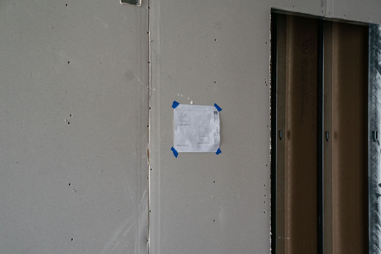 A small piece of paper taped to a gray wall next to a brown door in an unfinished space.