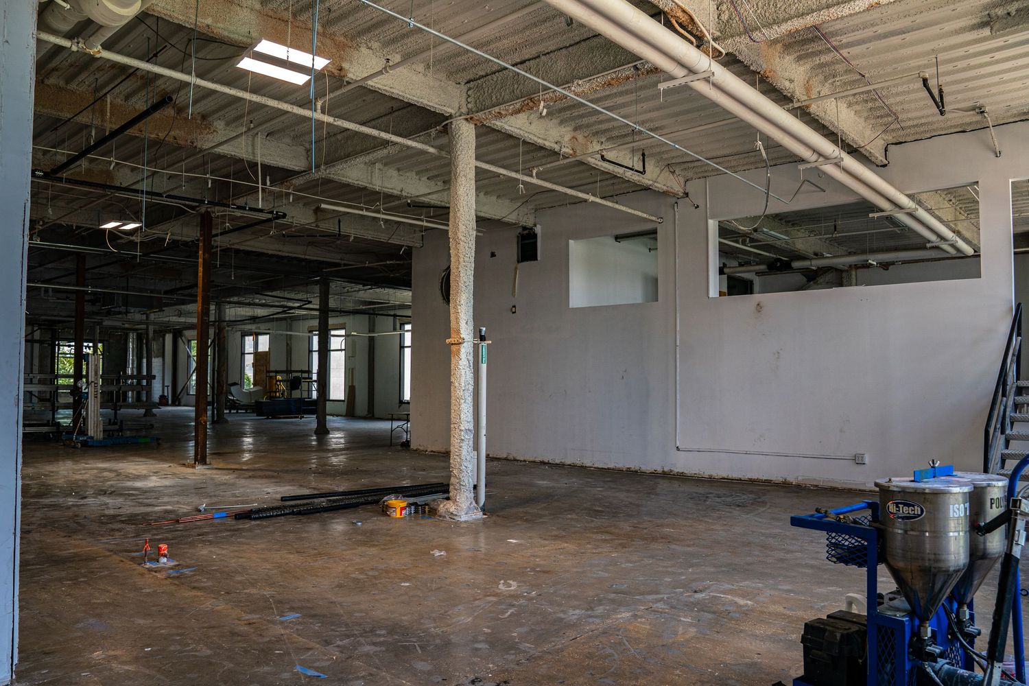 Empty industrial facility showing concrete floors and exposed ceiling infrastructure.