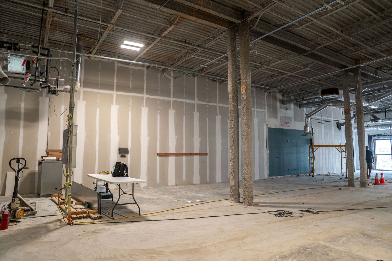 Empty commercial space undergoing renovation with exposed ceiling and support columns.