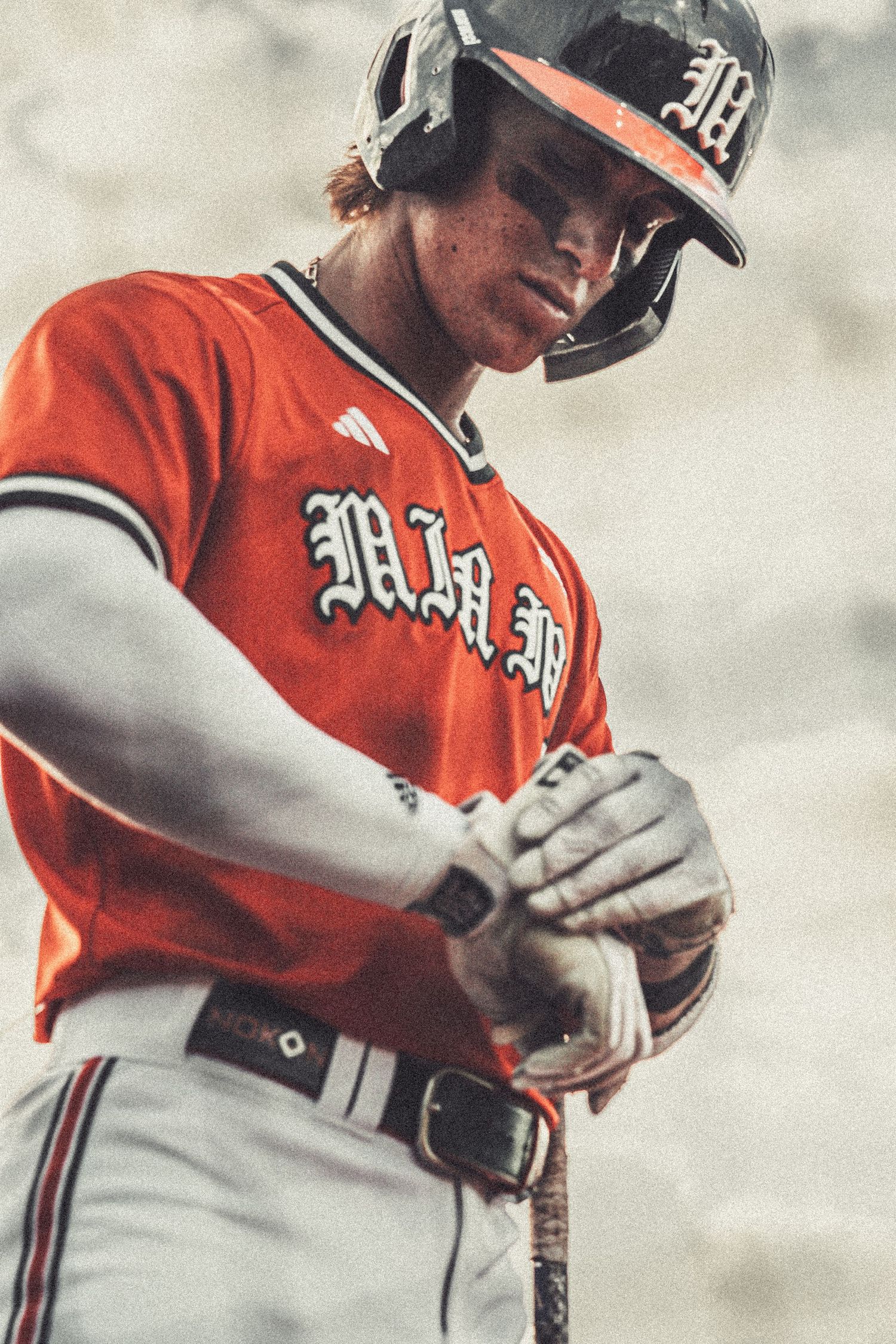 Baseball player in Miami Hurricanes orange uniform and helmet adjusting batting gloves at plate.