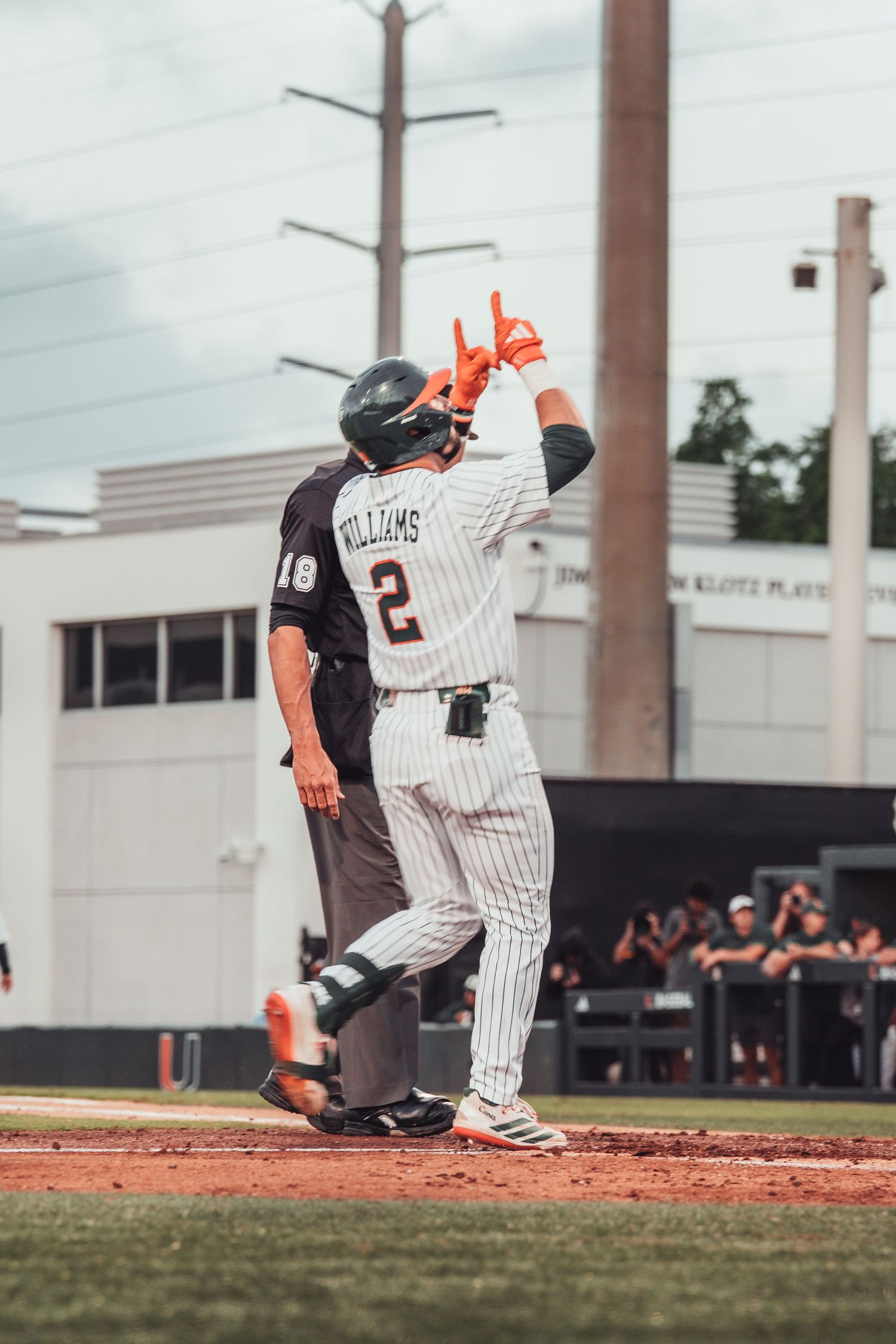 Baseball player Williams #2 celebrates at home plate wearing white pinstripe uniform with orange gloves, umpire visible behind.