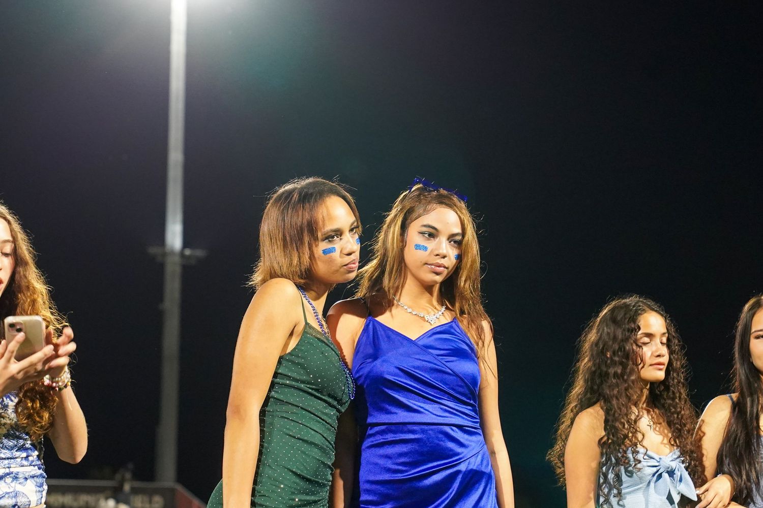 Students in formal dresses standing together under stadium lights.