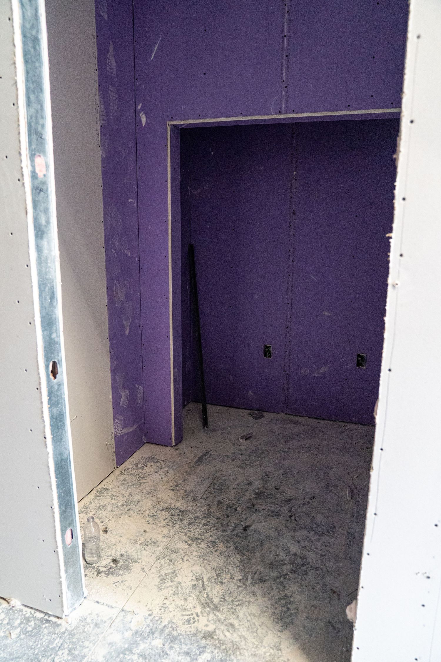 Purple-walled room under construction with exposed drywall and concrete floor.