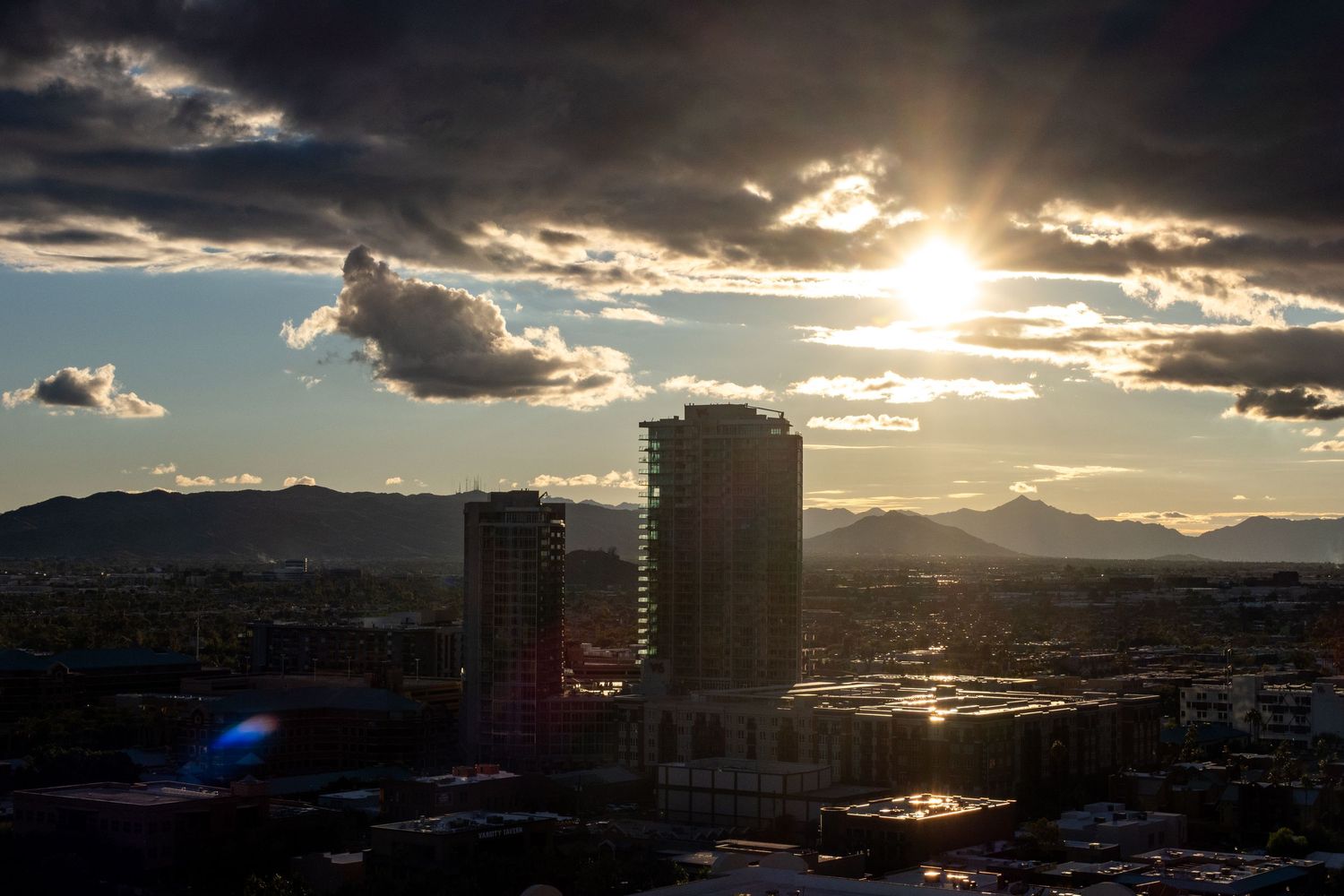 Urban cityscape at dusk with tall buildings silhouetted against a cloudy golden sky.