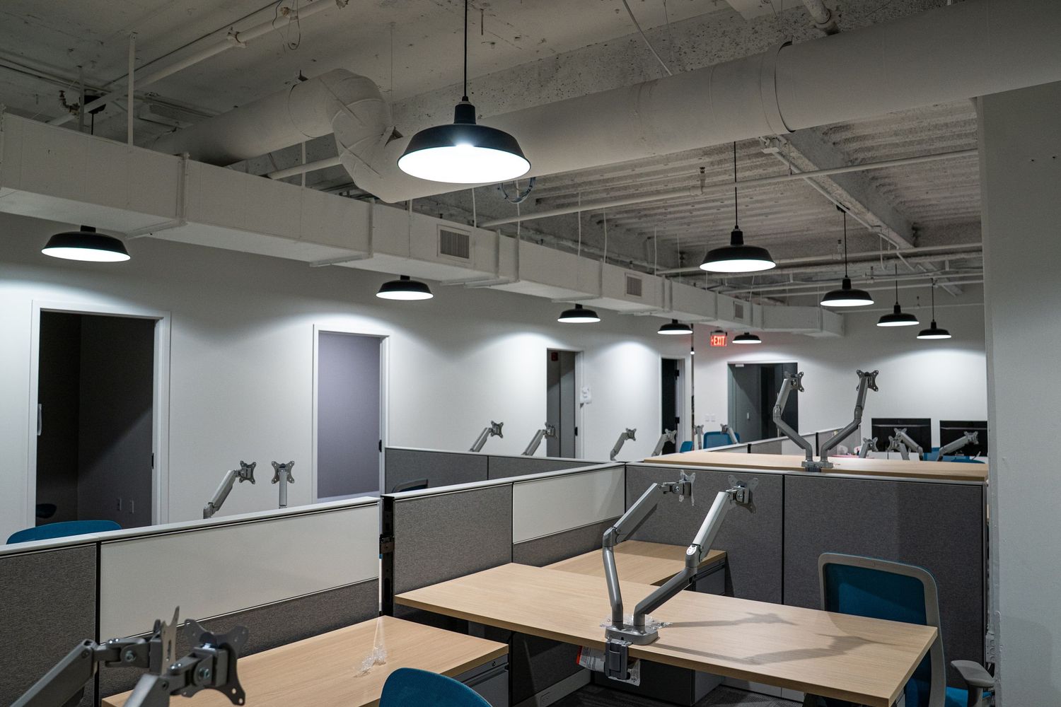 Commercial office interior featuring industrial lighting and gray cubicle partitions in an open floor plan.
