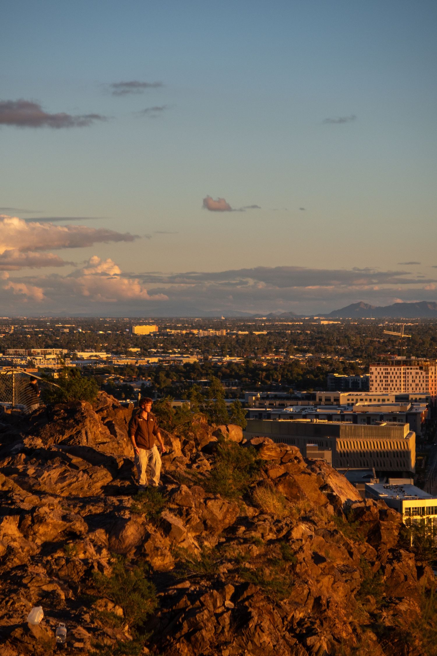 Urban skyline view during golden hour with dramatic clouds and rocky terrain.
