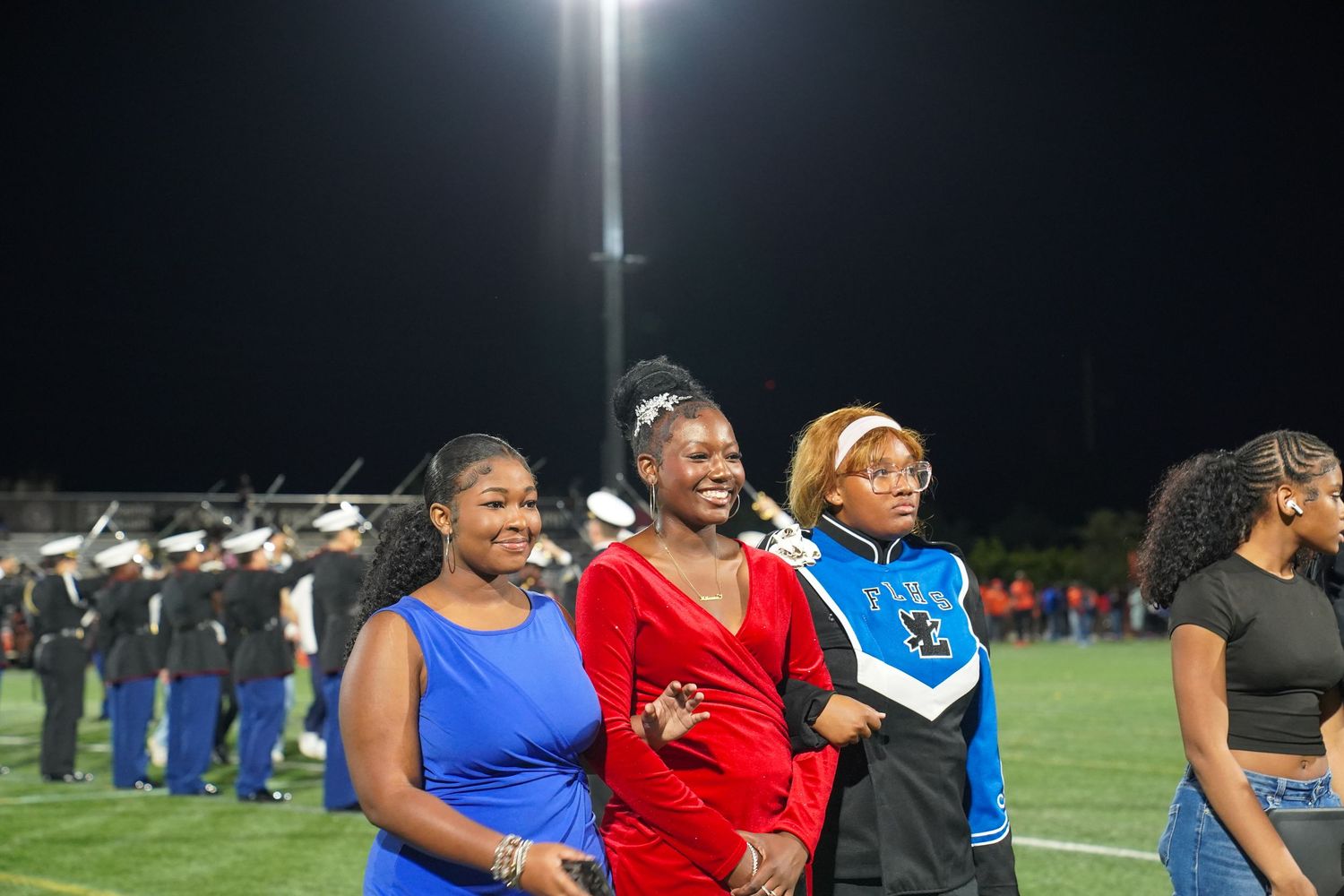 People in colorful uniforms stand together on a sports field under bright stadium lighting.