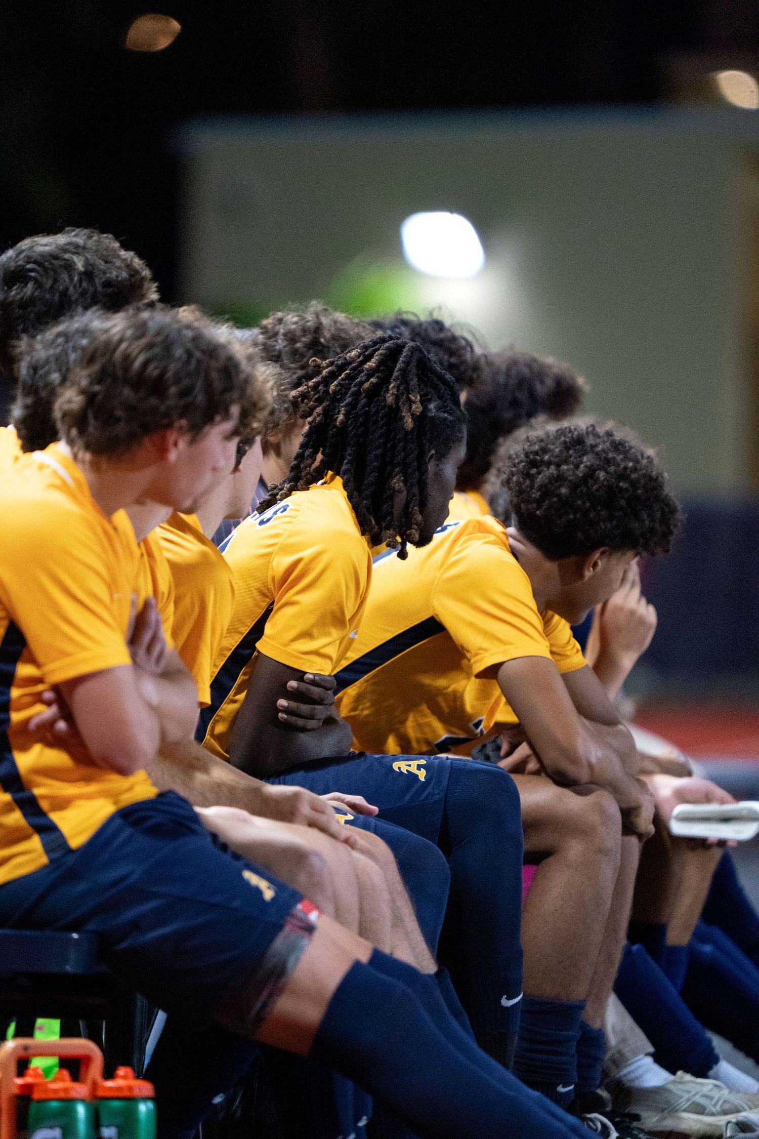 Team members in yellow and navy uniforms sit together on the sidelines during a game break.