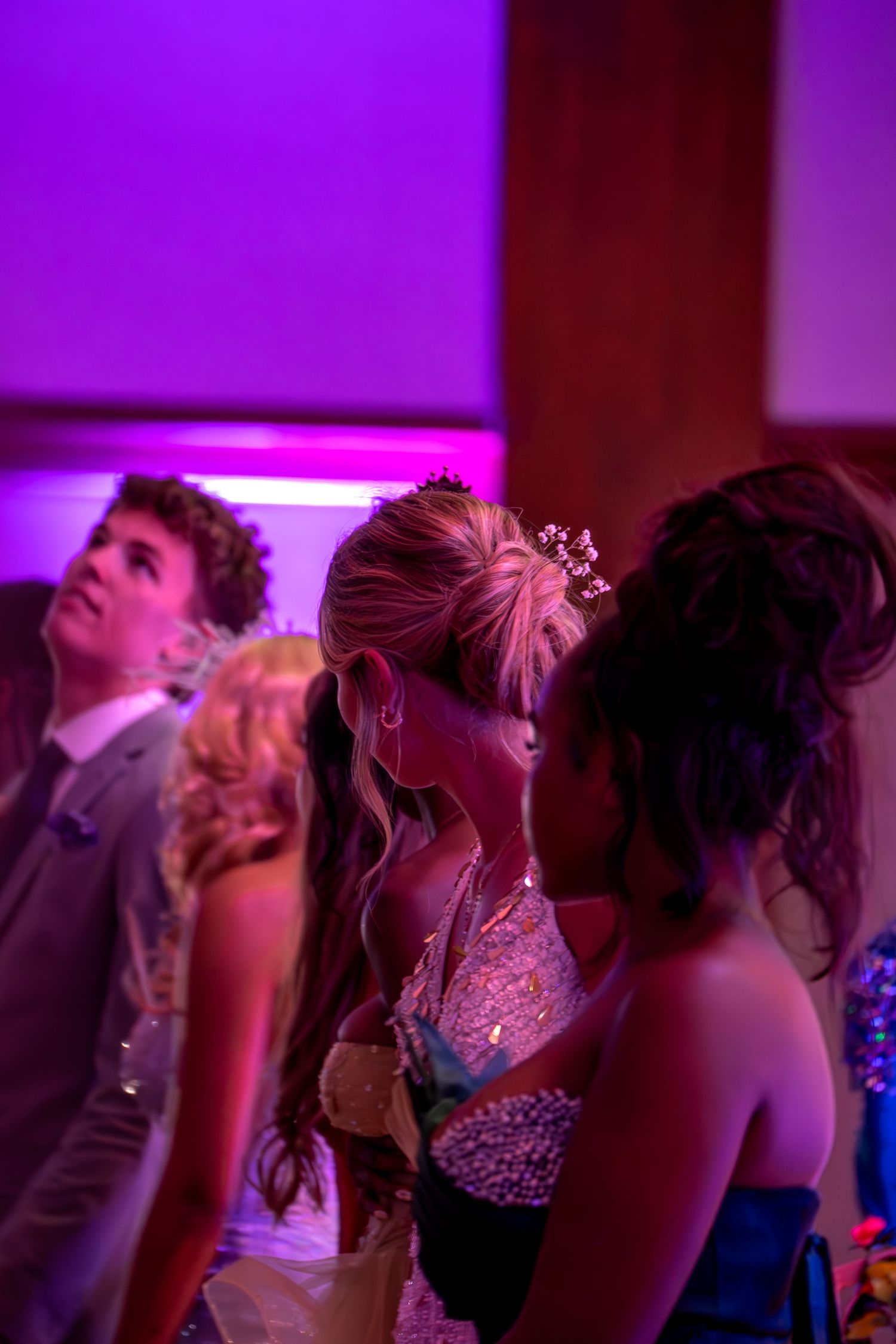Formal dance event with purple ambient lighting shows attendees in elegant dresses.