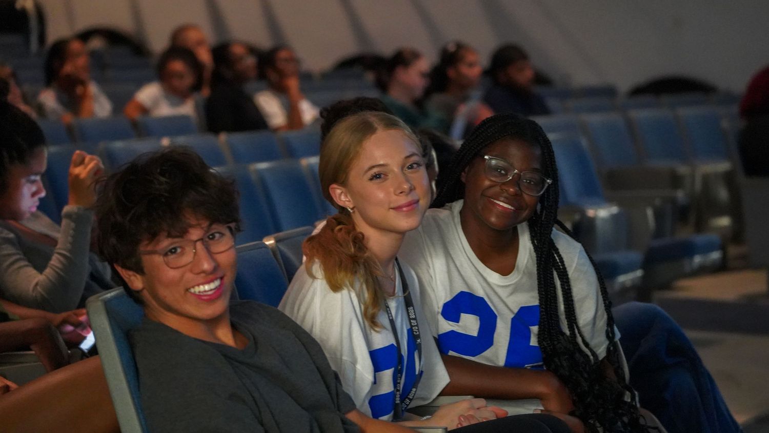 Students in sports jerseys enjoying a show in theater seating.