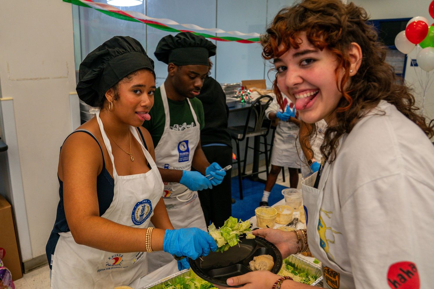 People wearing white aprons prepare food at serving stations.