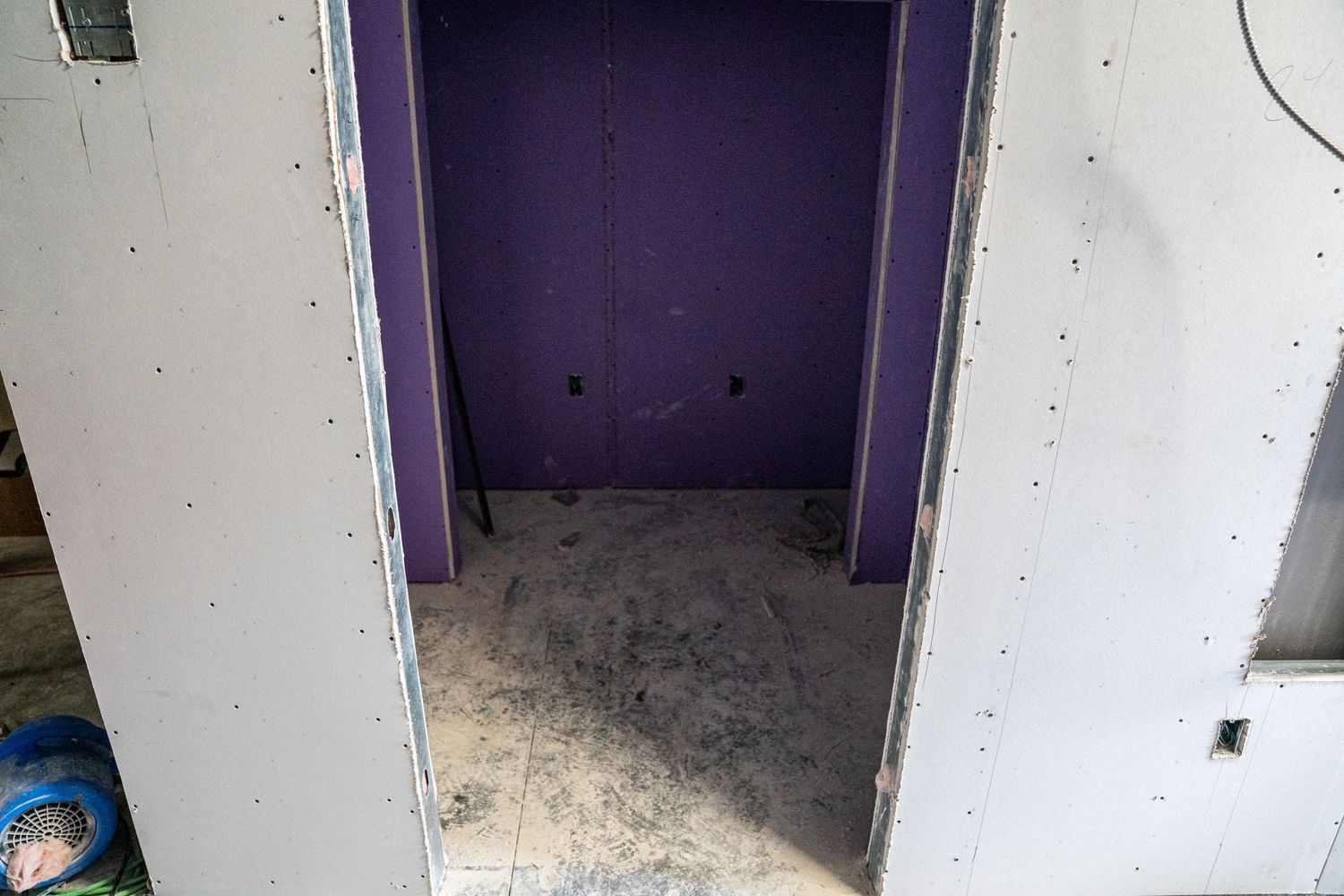 Empty room with purple accent wall and construction debris on concrete floor.