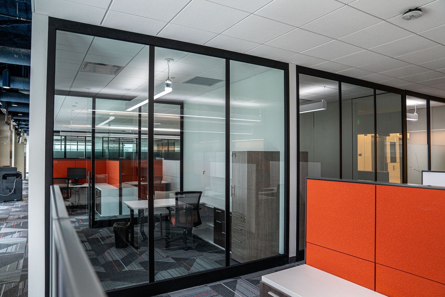 Professional office interior with orange accent walls, glass partitions, and contemporary workspace design.