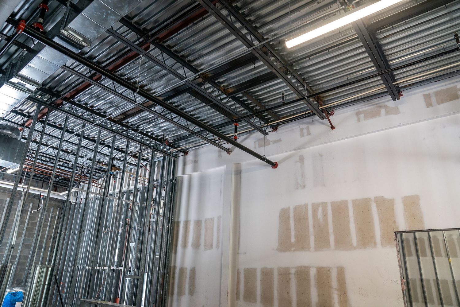 Drywall installation in progress with metal framing and exposed ceiling in commercial space.