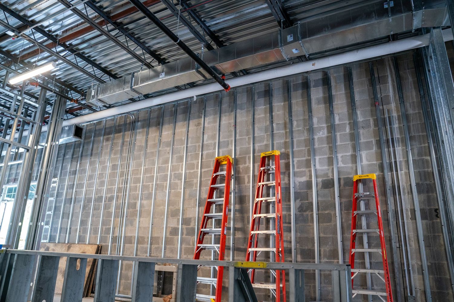 Metal framing installation in progress with ladders positioned along unfinished walls.