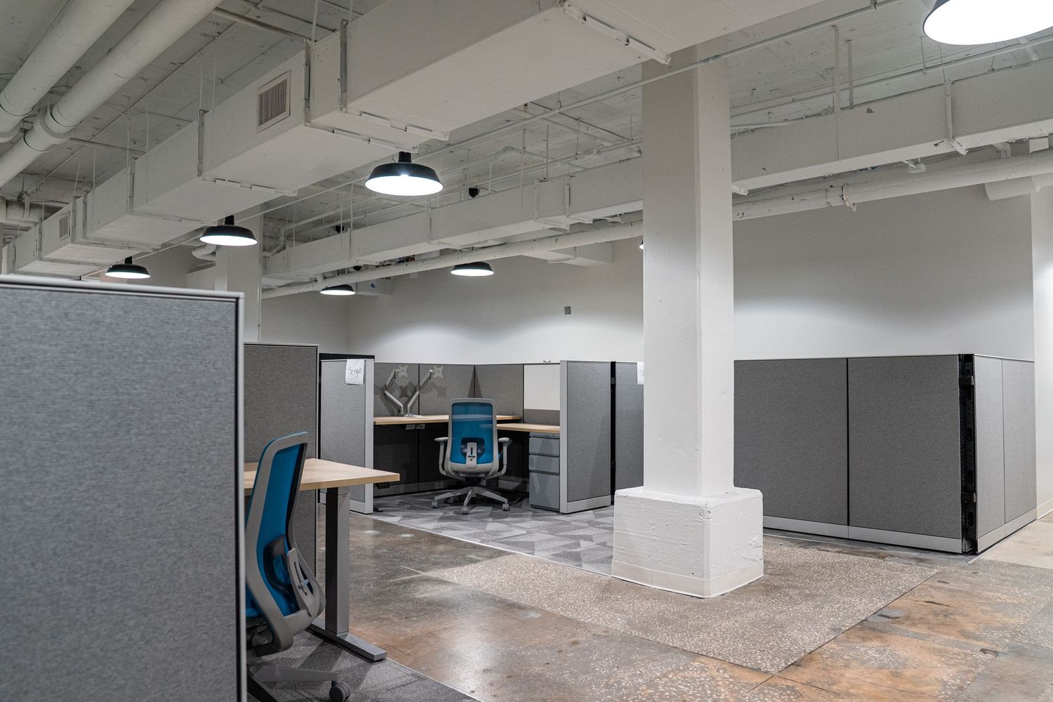 Large open concept office with industrial lighting fixtures and gray modular workstations.