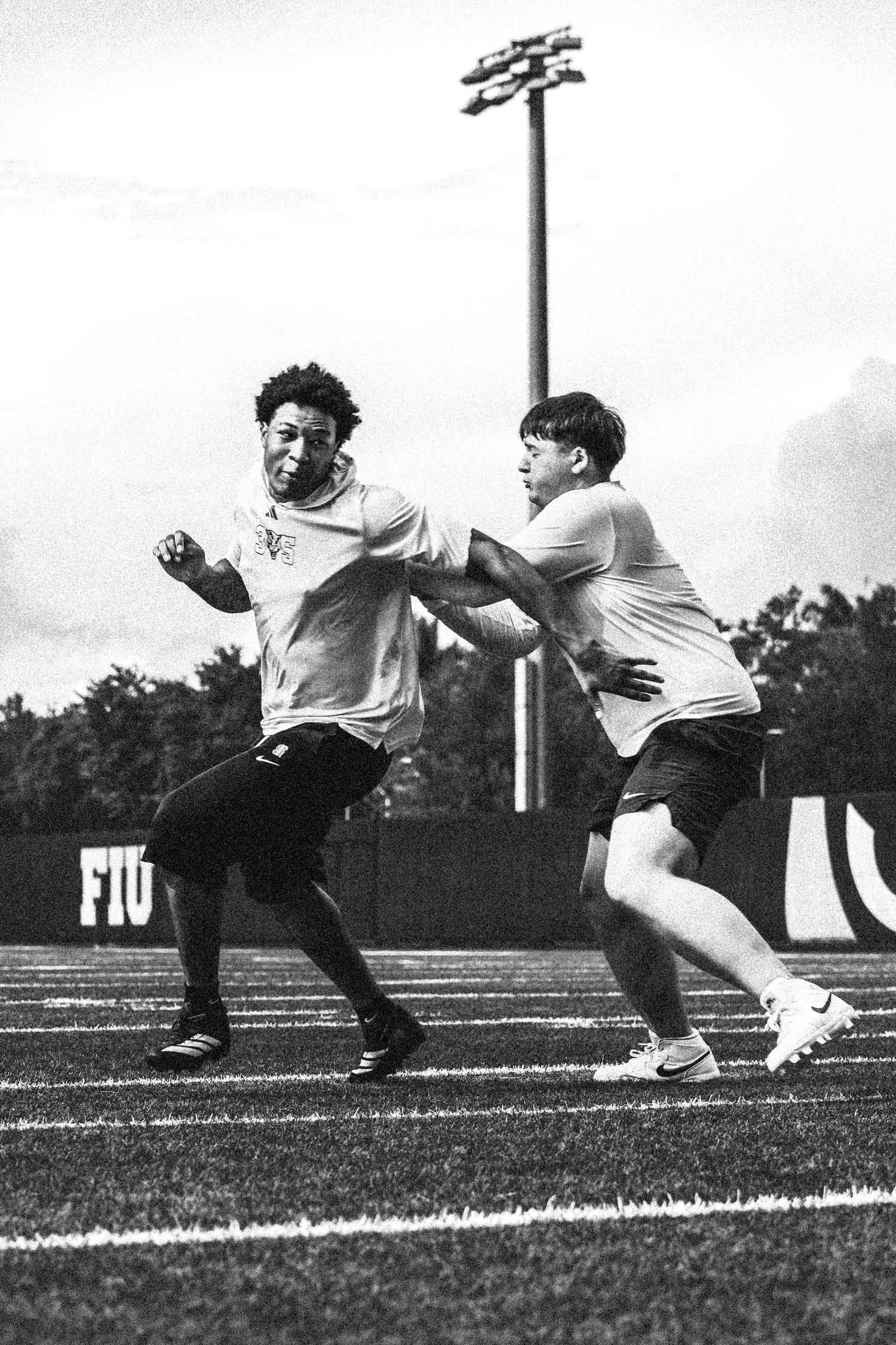 Two football players practice blocking drills on an FIU athletic field in this black and white action photo.