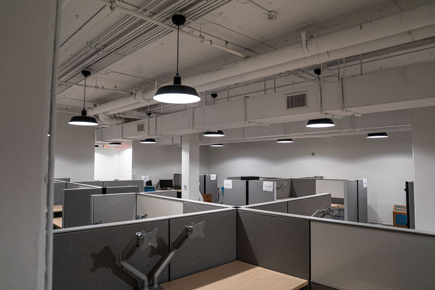 Spacious commercial office interior with black pendant lights and gray cubicle dividers.